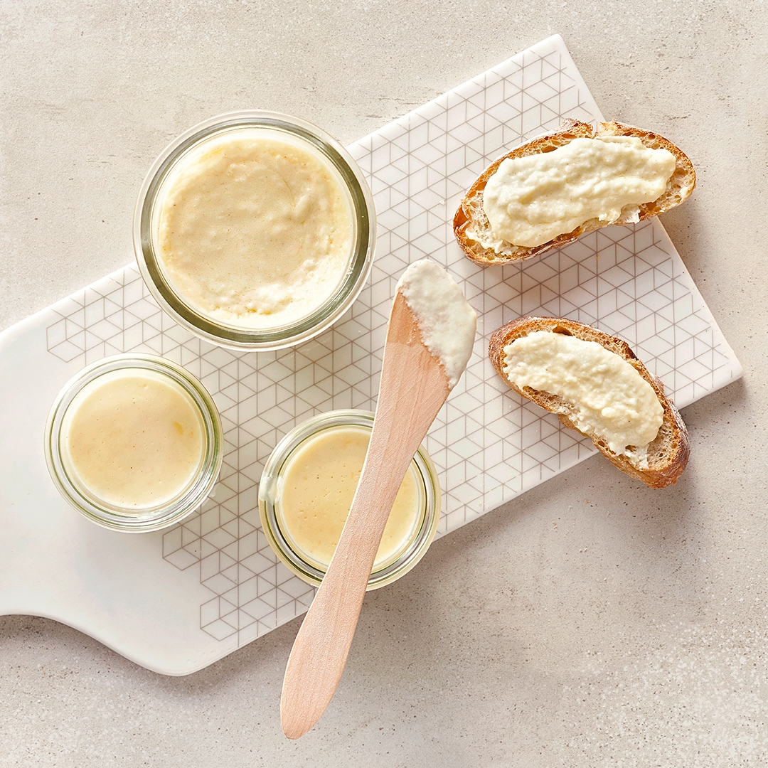 Kleine Glasschüsseln auf einem Brett, gefüllt mit heller Creme, daneben zwei Stücke Brot, bestrichen mit der hellen Creme