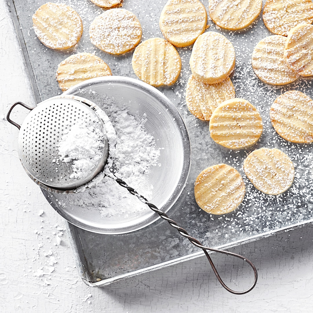 Blech mit sehr kleinen dünnen Plätzchen, mit Puderzucker bestäubt
