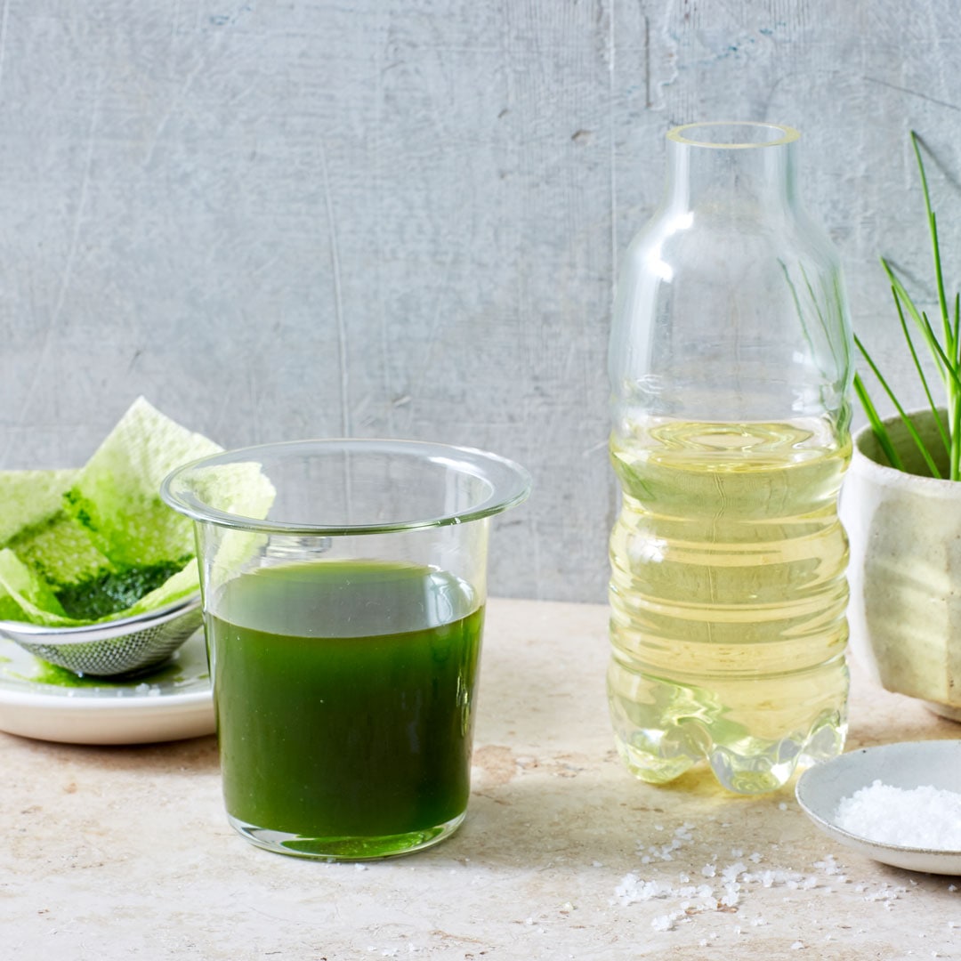 Gläserner Behälter mit grüner Flüssigkeit, daneben Flasche mit Öl und Schnittlauch