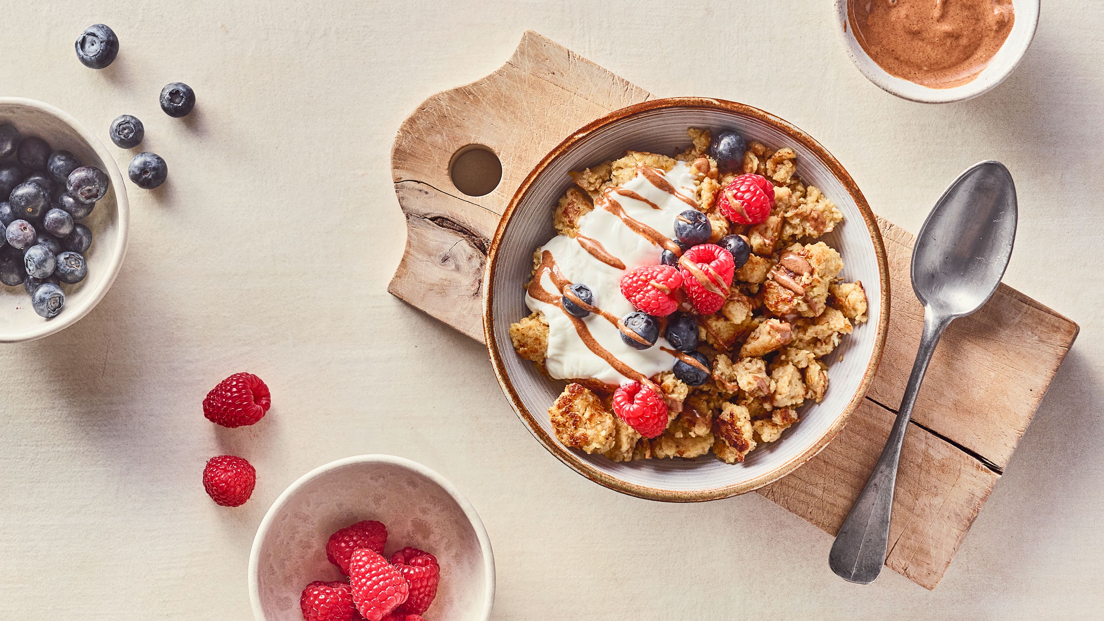 Rezept für Scrambled Oats Eine Schale mit Teigstückchen, getoppt mit Joghurt, frischen Blaubeeren, frischen Himbeeren und Nussmuss