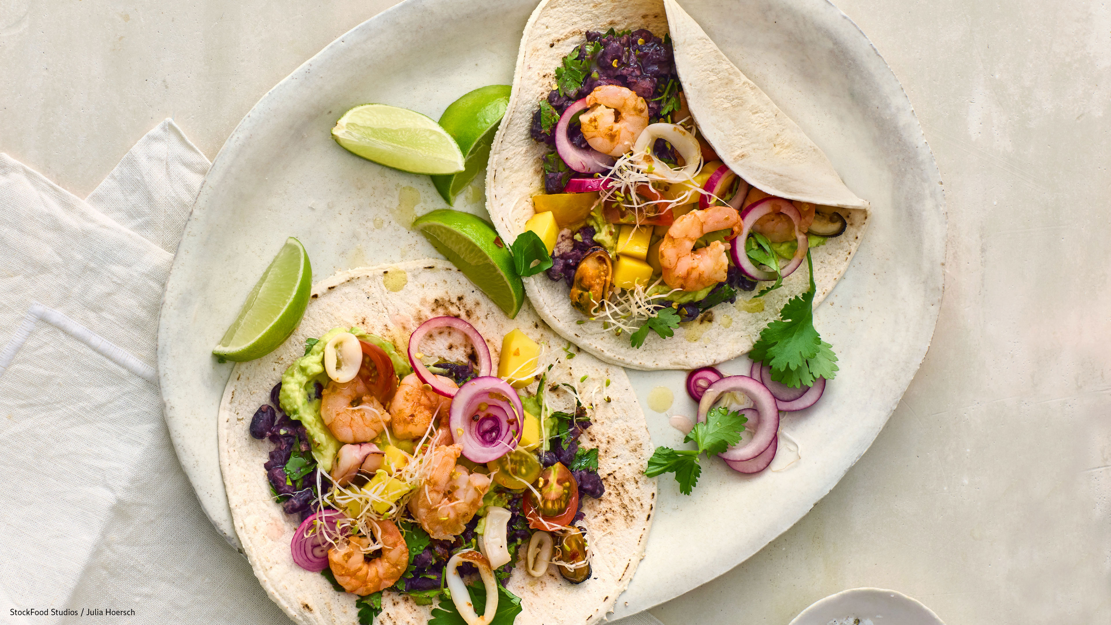 Rezept für Seafood Tacos aus dem Airfryer Mit Garnelen und buntem Gemüse gefüllte Weizenfladen auf Teller