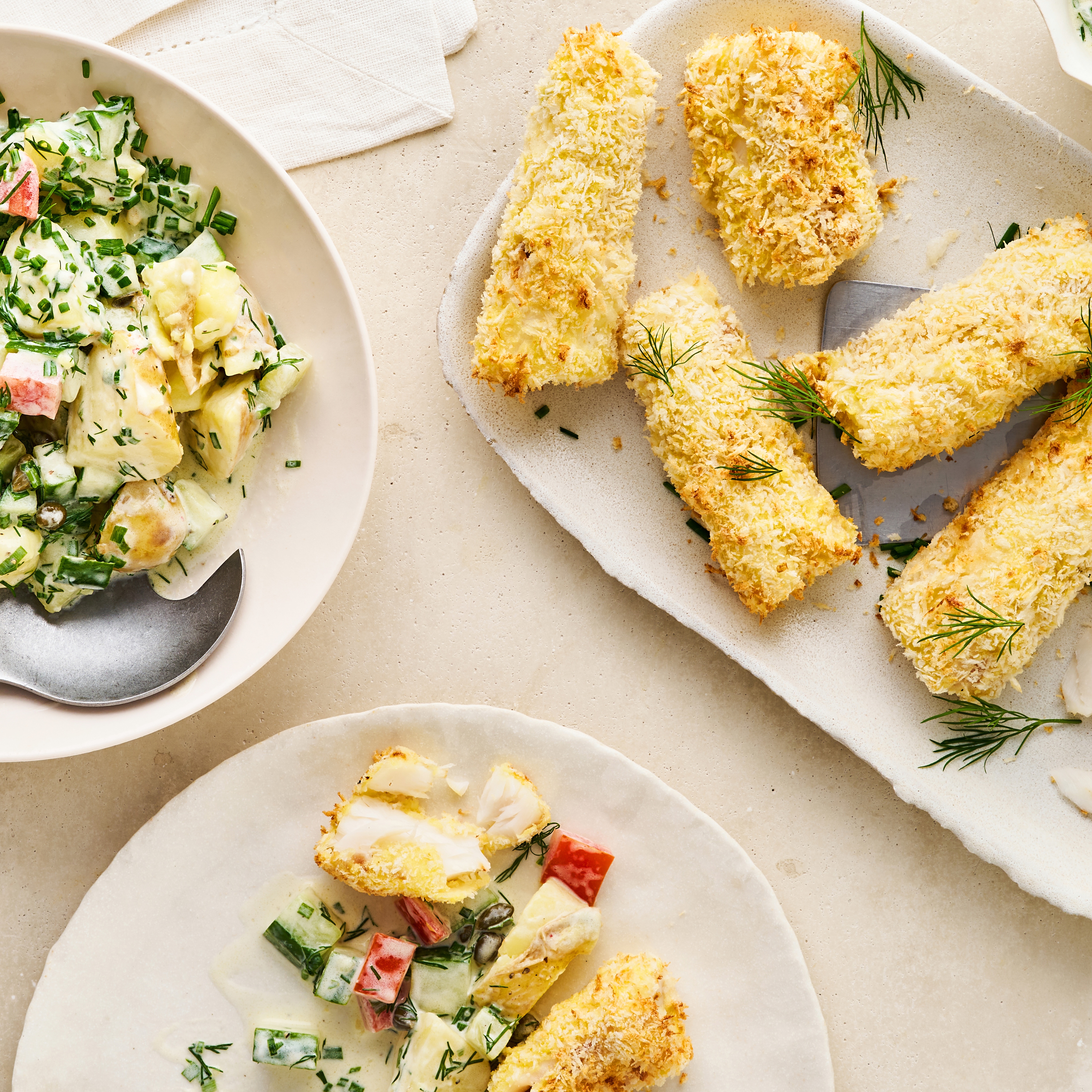 Teller mit frittierten Fischstückchen und einem Salat mit Gurke, Paprika und heller Soße mit frischem Schnittlauch und frischem Dill