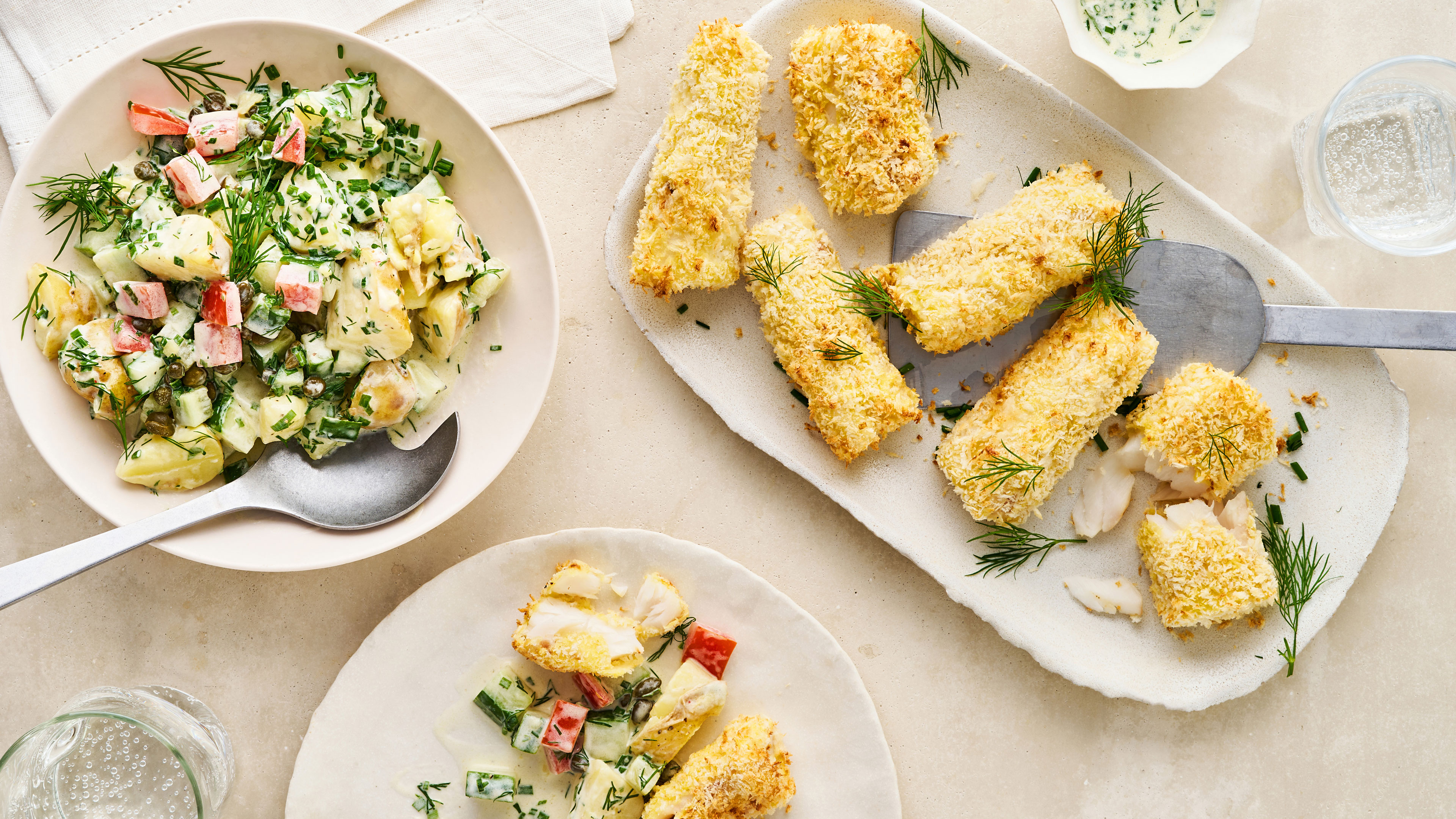 Teller mit frittierten Fischstückchen und einem Salat mit Gurke, Paprika und heller Soße mit frischem Schnittlauch und frischem Dill