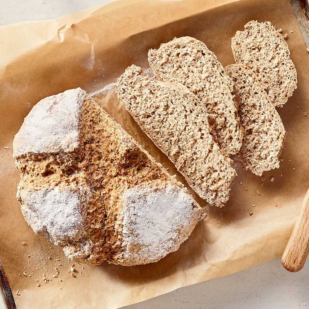 Ein Blech mit einem runden, aufgeschnittenen Brotlaib, mehreren hellbraunen Brotscheiben und weißem Mehl auf der Kruste.