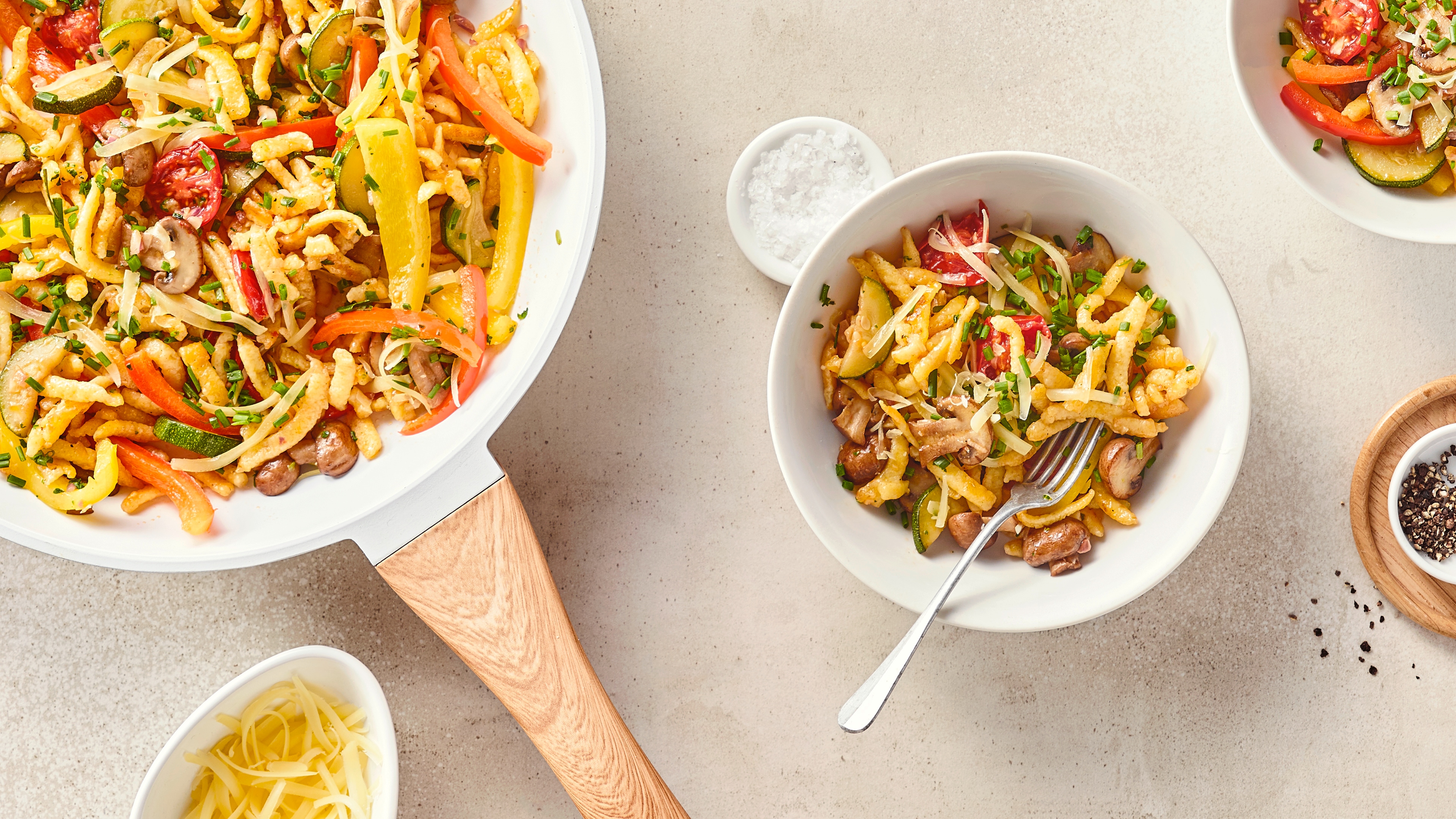 Rezept für Spätzlepfanne mit Gemüse Eine Pfanne mit Spätzle, Paprikastreifen, Kirschtomaten, Champignons und Zucchini, getoppt mit Schnittlauch und Reibekäse