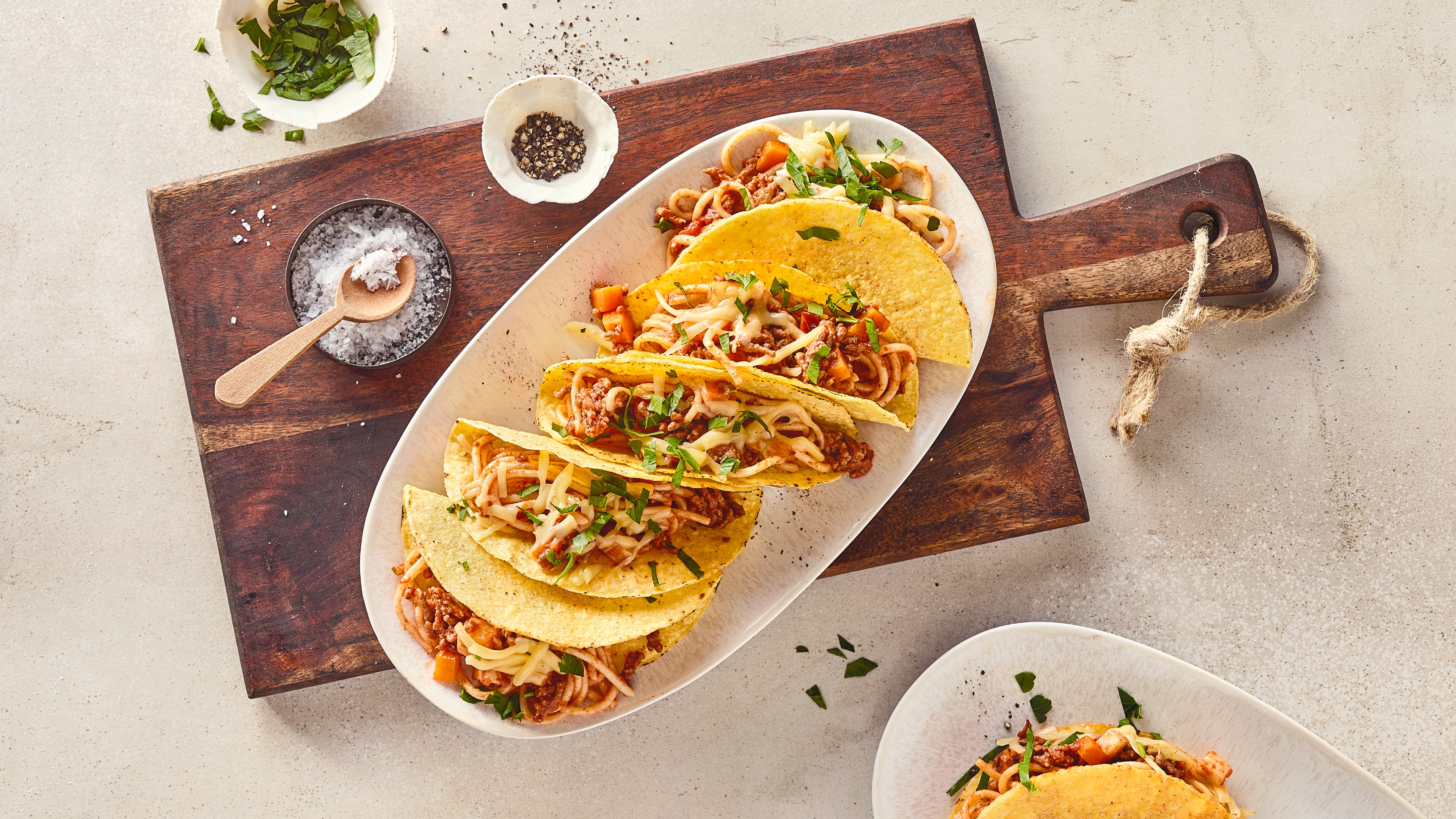 Rezept für Spaghetti Tacos mit Hackfleisch Ein ovaler Teller mit Tacoschalen, gefüllt mit Spaghetti und Hackfleisch, getoppt mit Streukäse und gehacktem Koriander