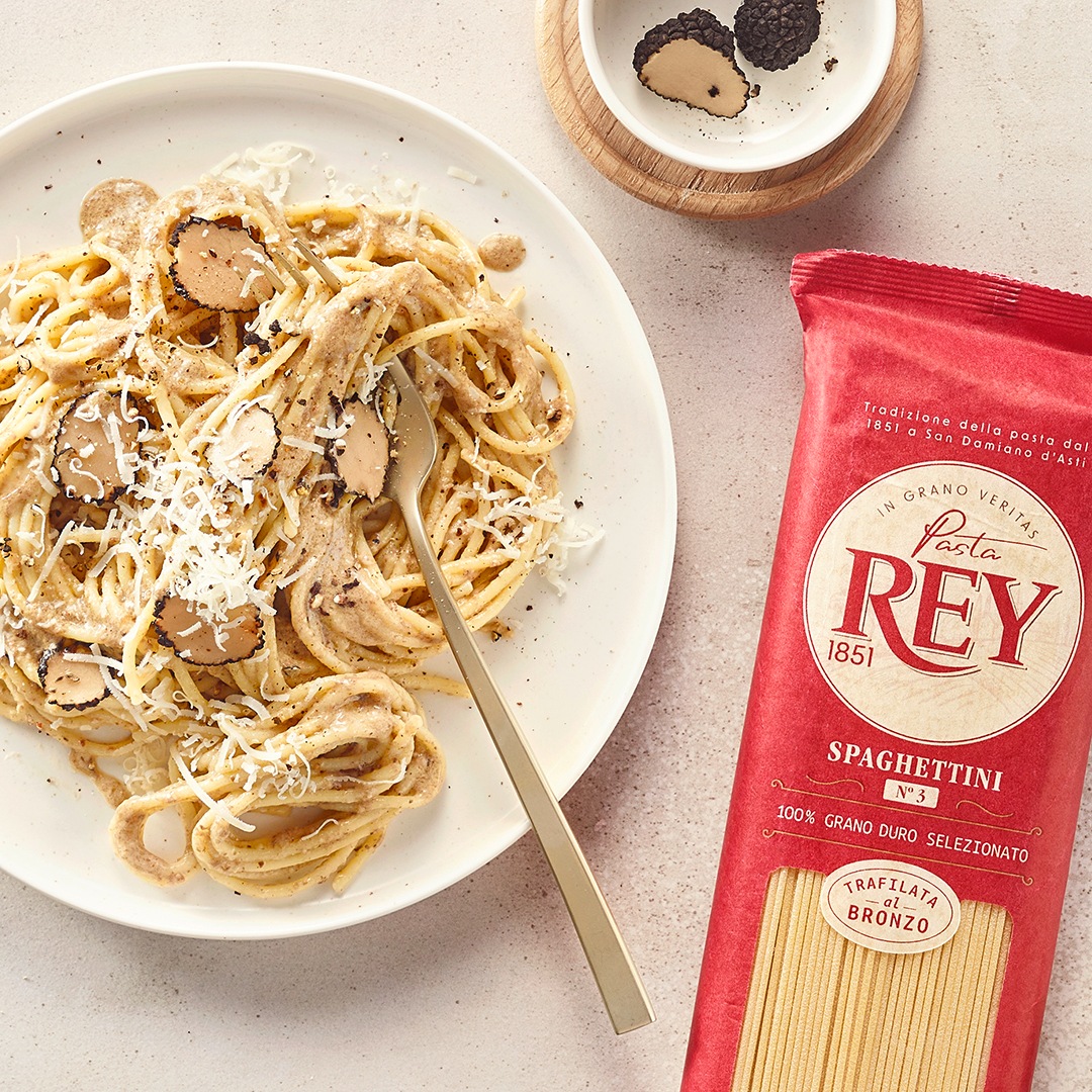 Teller mit Spaghetti, Trüffelscheiben und geriebenem Käse. Daneben eine Packung Pasta Rey Spaghettini