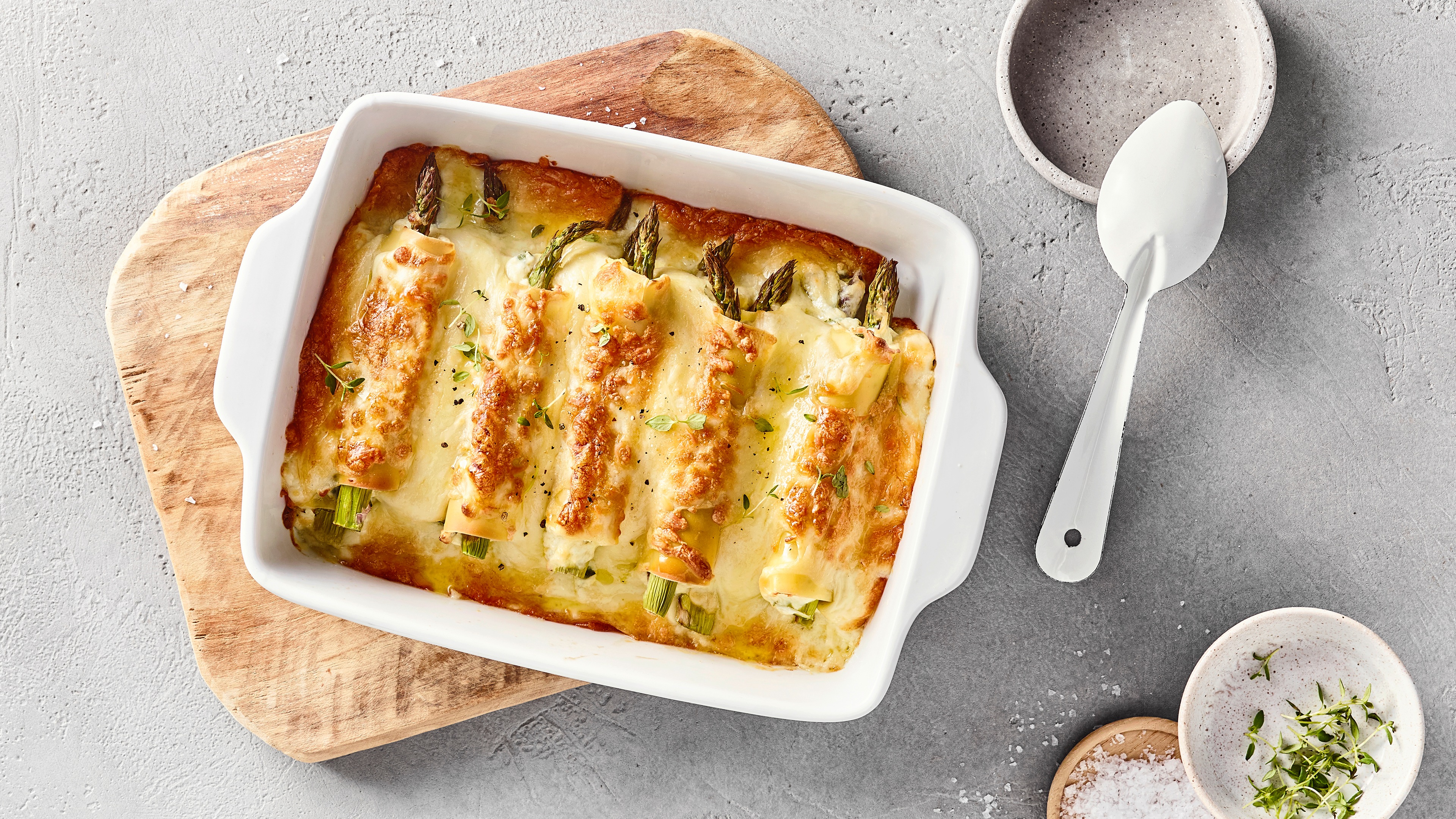 Auflaufform mit mit grünen Spargelstangen gefüllten Cannelloni Nudeln. Mit Käse überbacken