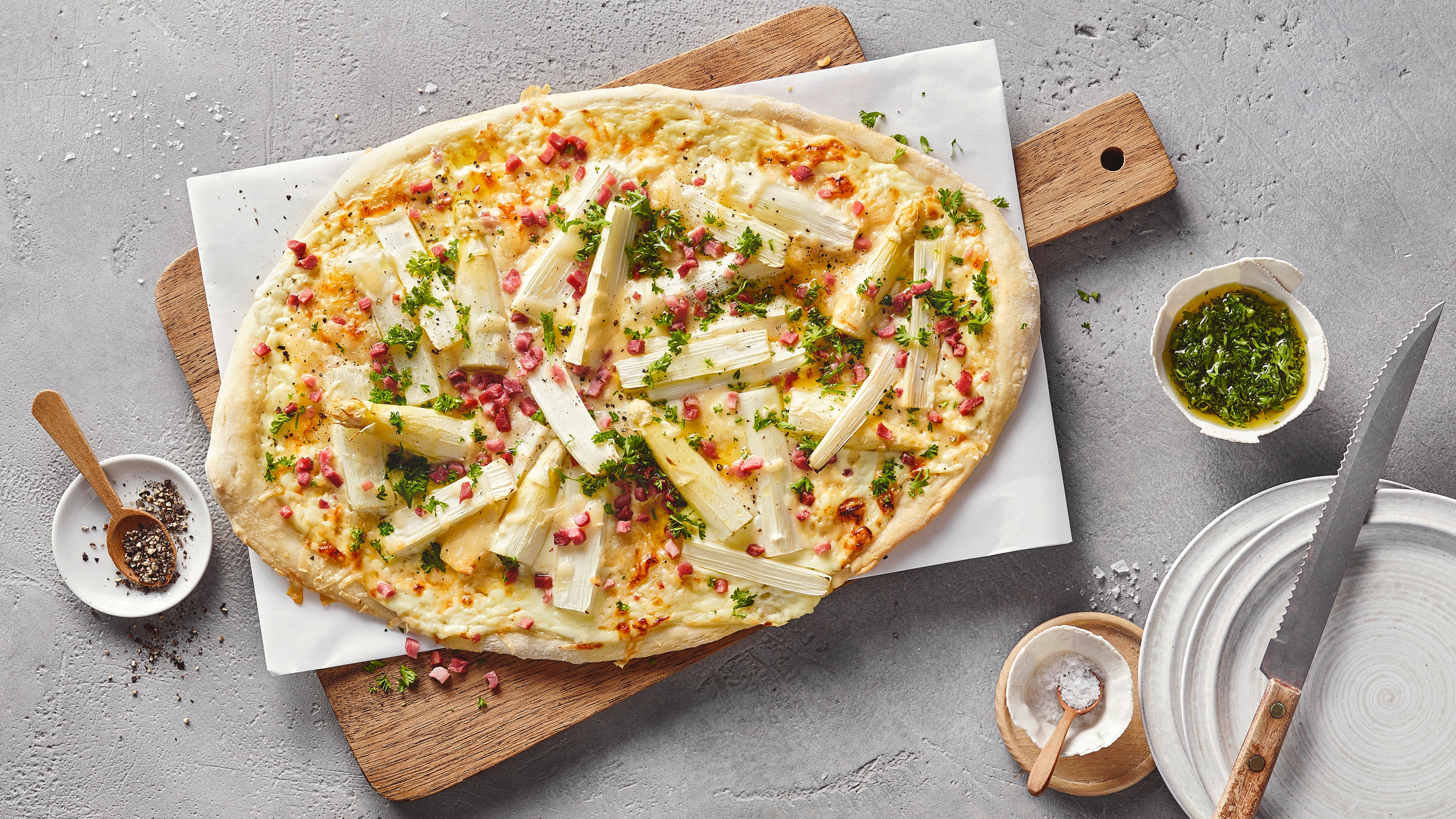Holzbrett mit Flammkuchen mit Spargel und Schinken.