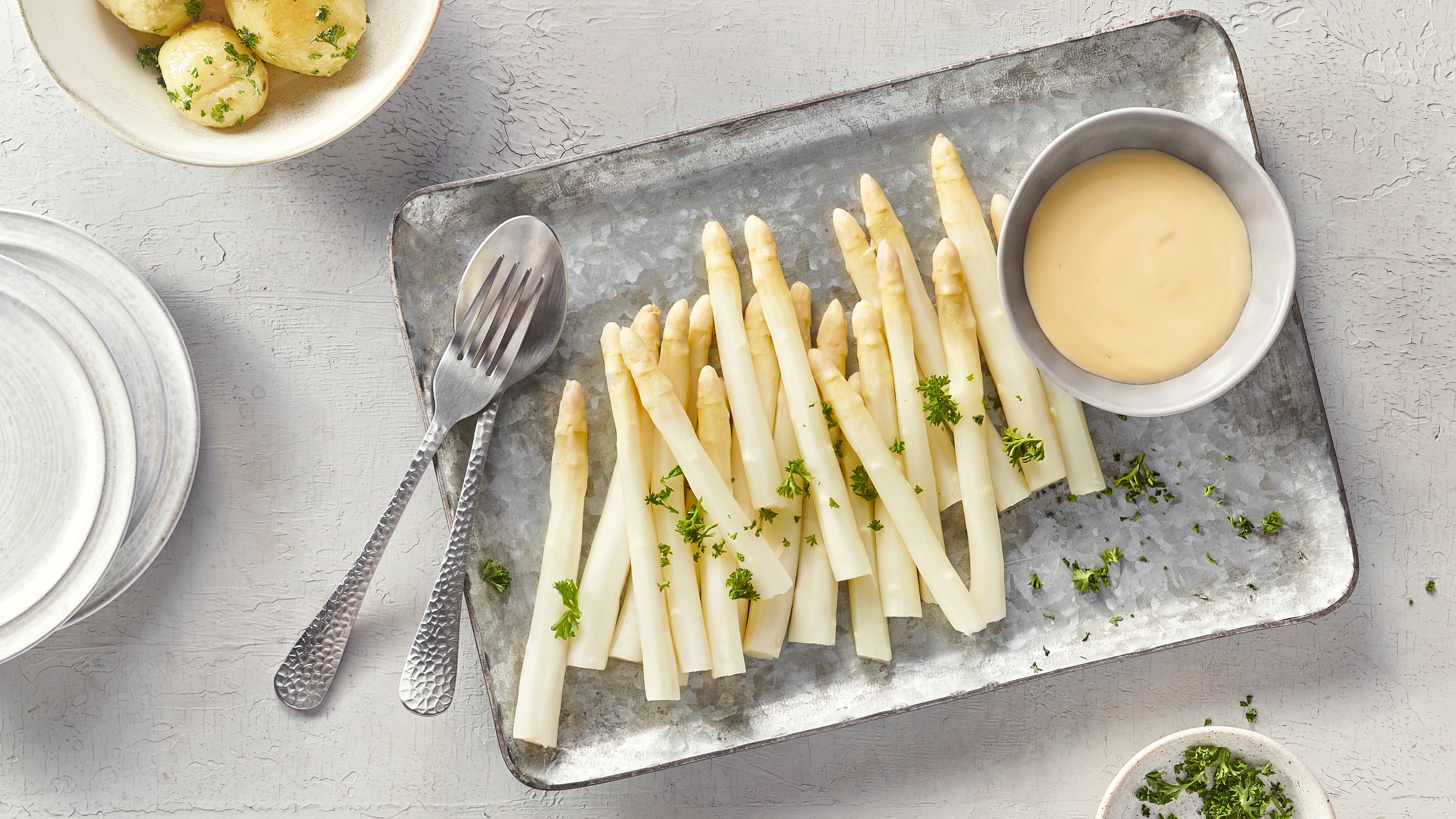 Kurze Spargelstangen auf Platte neben einem Schälchen mit heller cremiger Soße.
