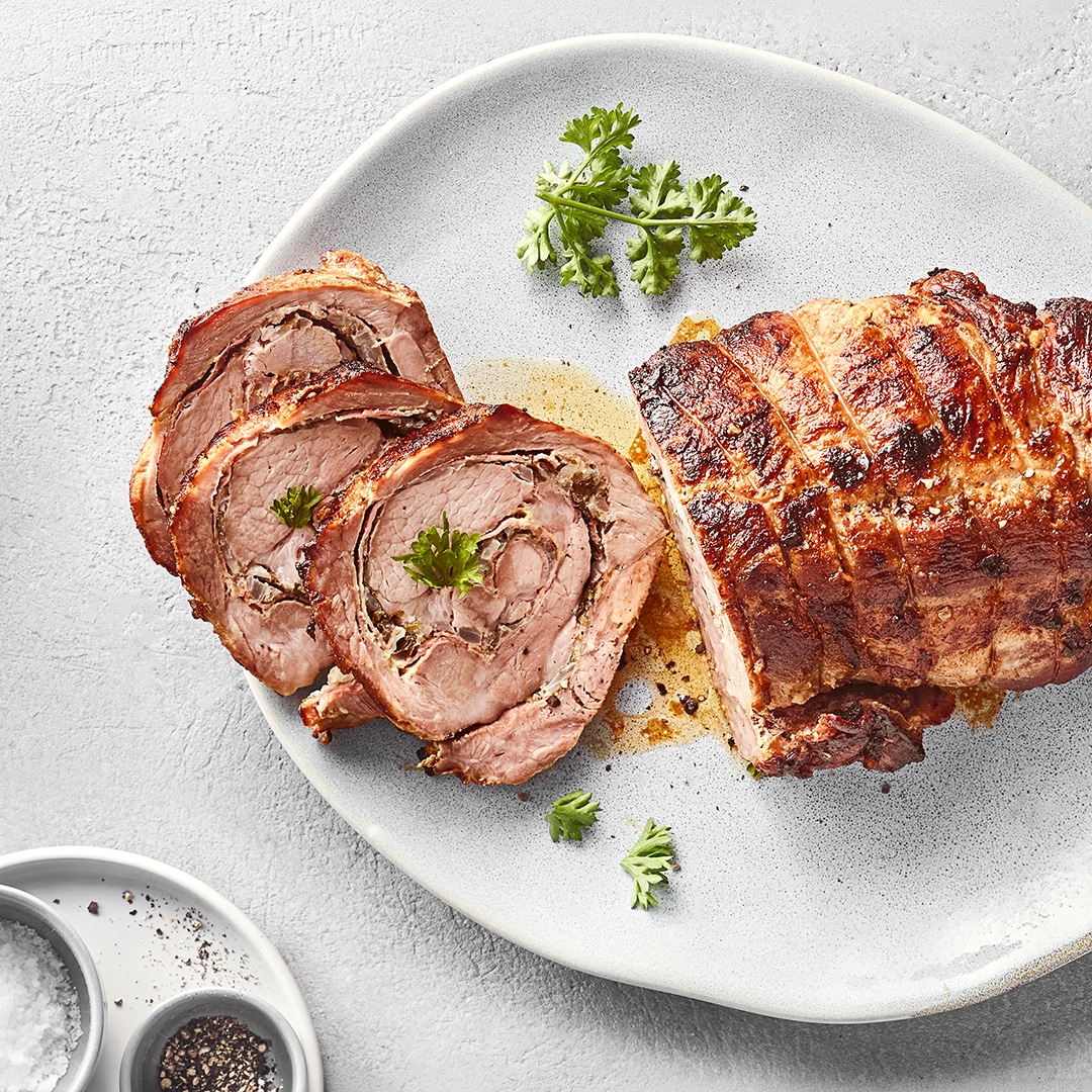Gebratener Rollbraten in Scheiben auf einer weißen Platte, garniert mit Petersilie.