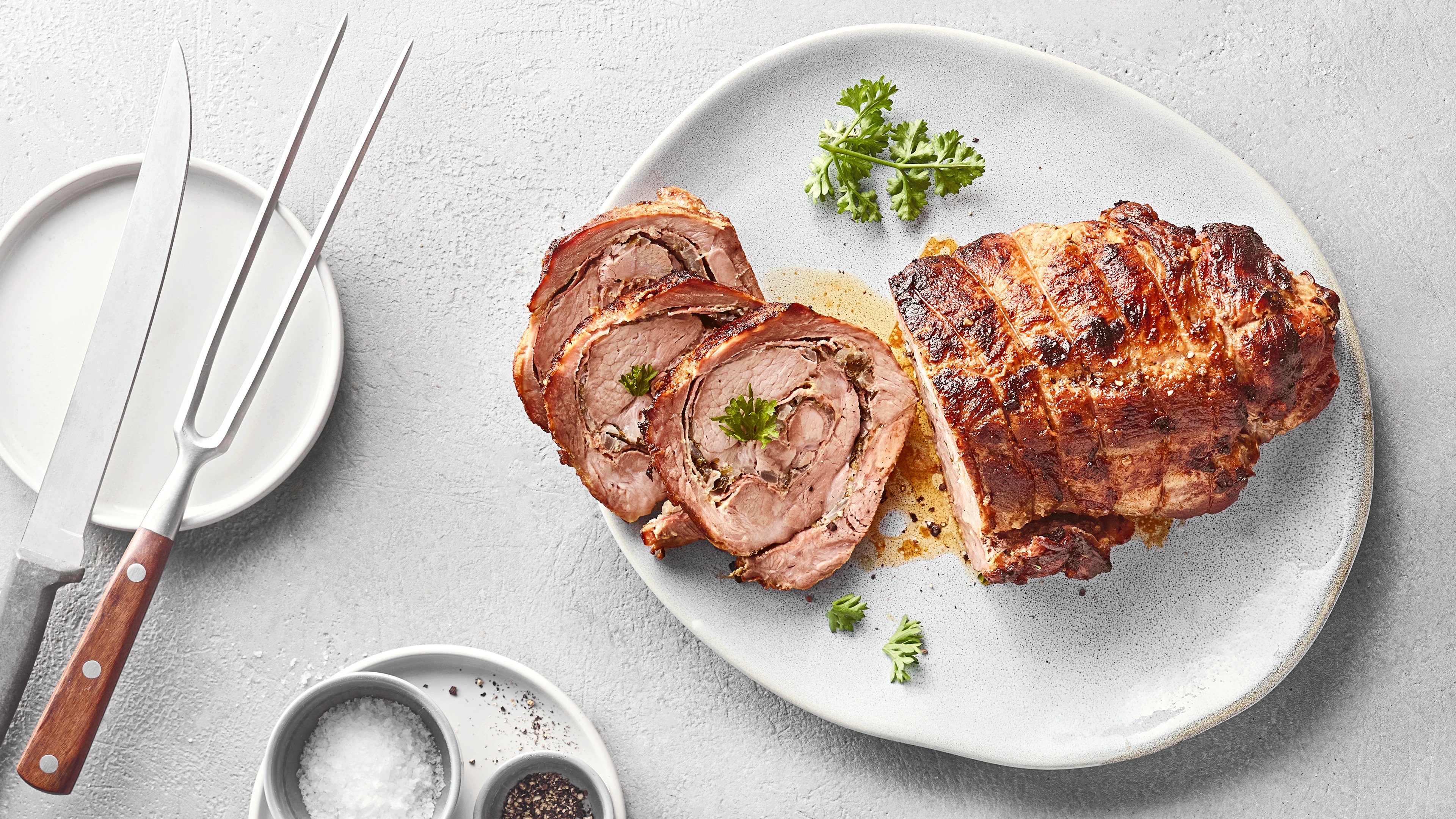 Gebratener Rollbraten in Scheiben auf einer weißen Platte, garniert mit Petersilie.