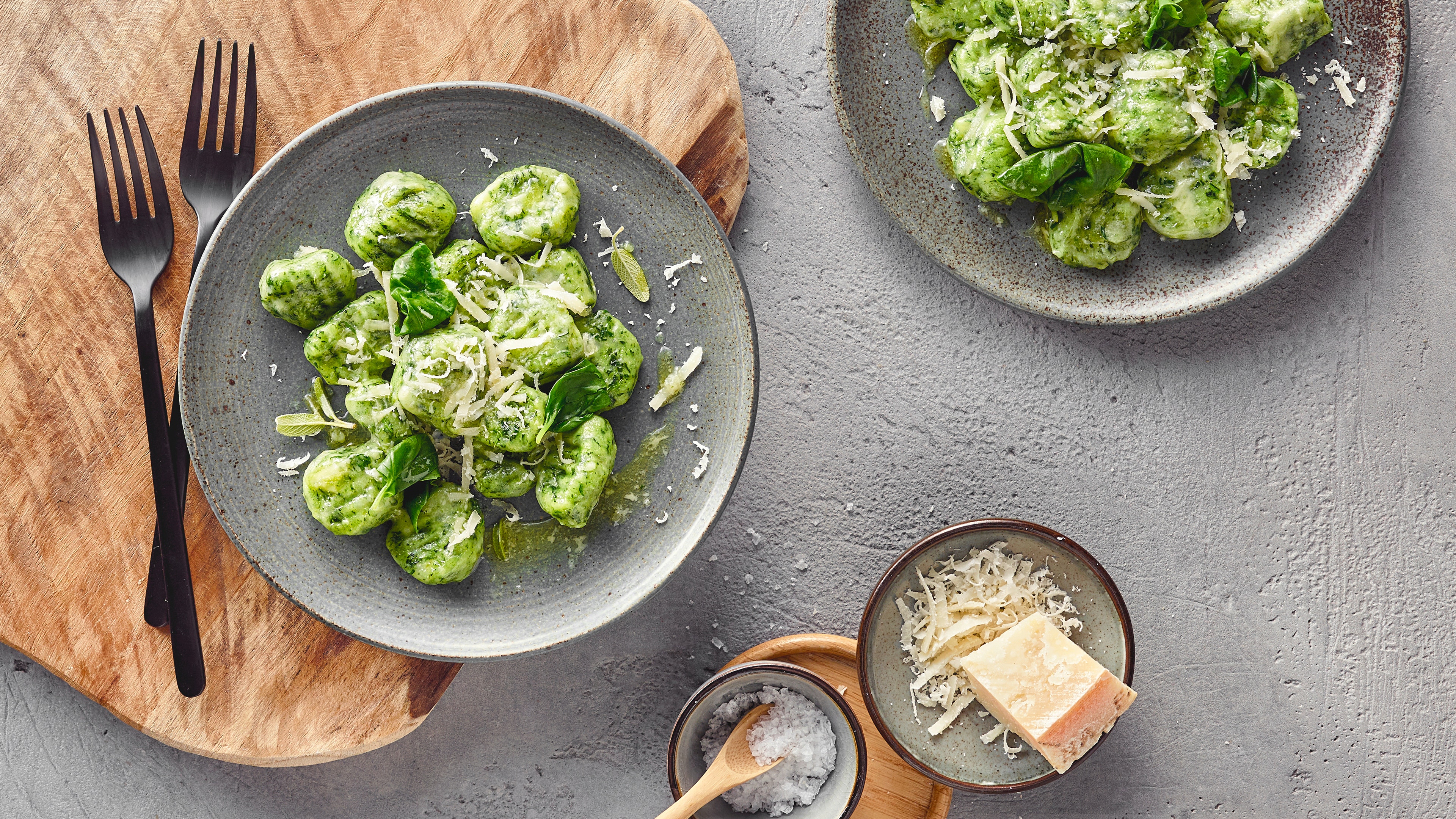 Rezept für Spinatgnocchi Ein Teller mit grünen Gnocchi, bestreut mit geriebenem Käse und frischem Basilikum, daneben eine Schale mit grobem Salz