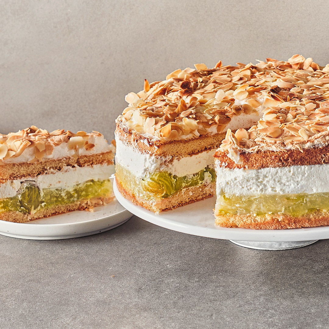 Eine Torte aus fluffigen hellen Böden, luftiger Creme und einer Fruchtschicht, getoppt mit Baiser und gehobelten Mandeln