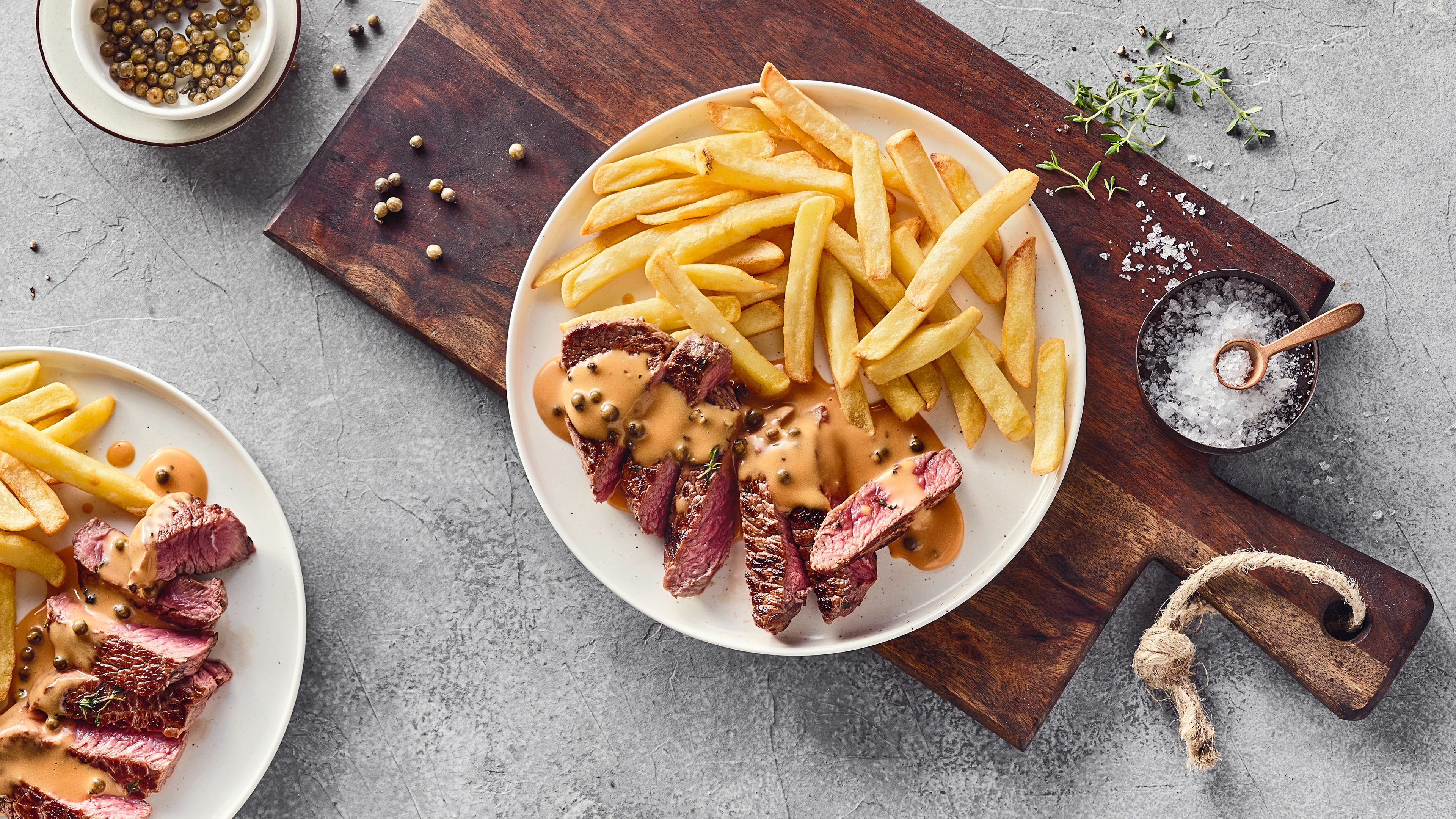Rezept für Steak au poivre Ein Teller mit saftigen Fleischstücken, in der Mitte leicht rosa, getoppt mit heller Soße mit Pfefferkörnern, dazu knusprige Pommes