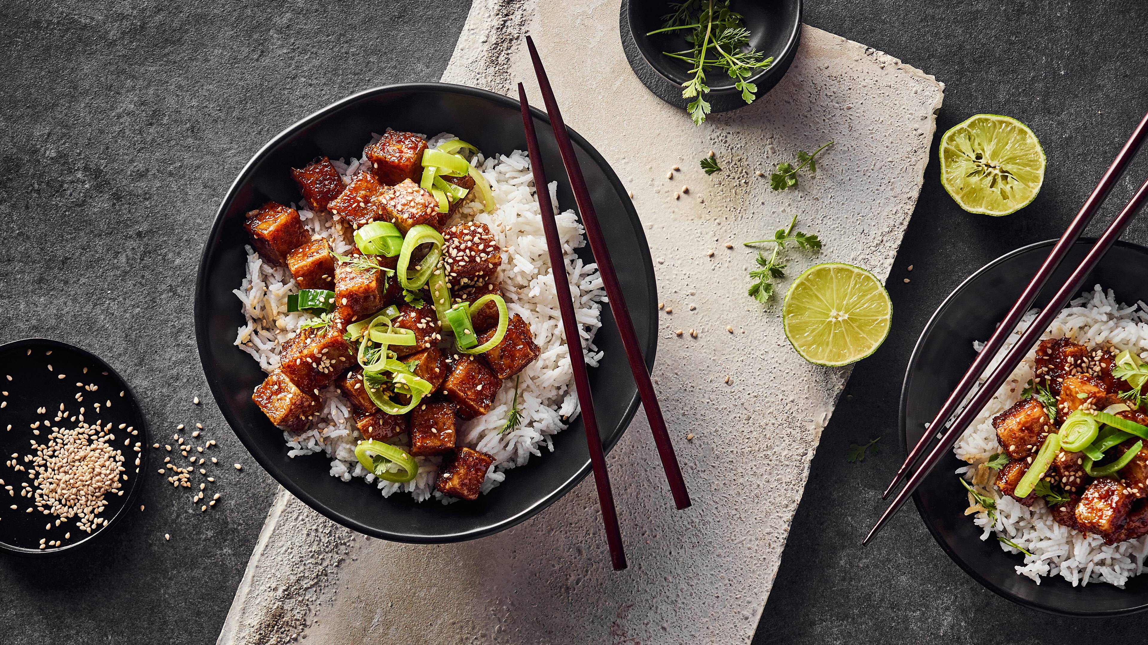 Rezept für Sticky Tofu Eine Schale Basmatireis, getoppt knusprig-karamellisierten Tofuwürfeln, garniert mit Frühlingszwiebeln und Sesam