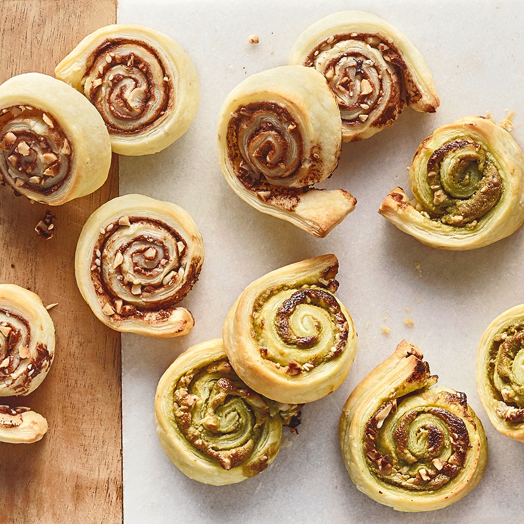 Ein Brett mit gebackenen Blätterteig Röllchen, gefüllt mit Pistazien- und Schokocreme.