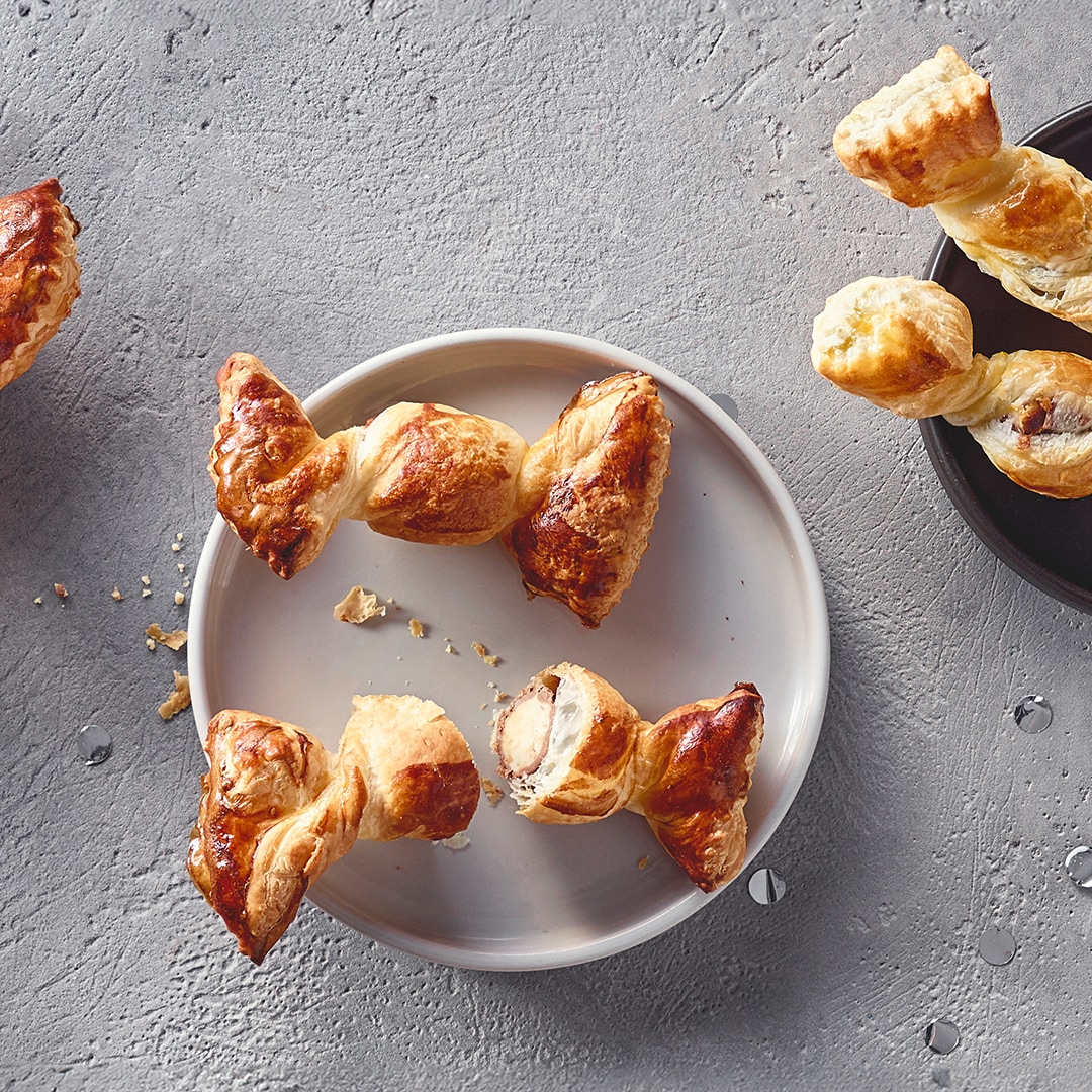 Ein Teller mit gedrehten Blätterteigstücken, goldbraun gebacken und gefüllt mit einer hellen Creme, daneben einige Krümel