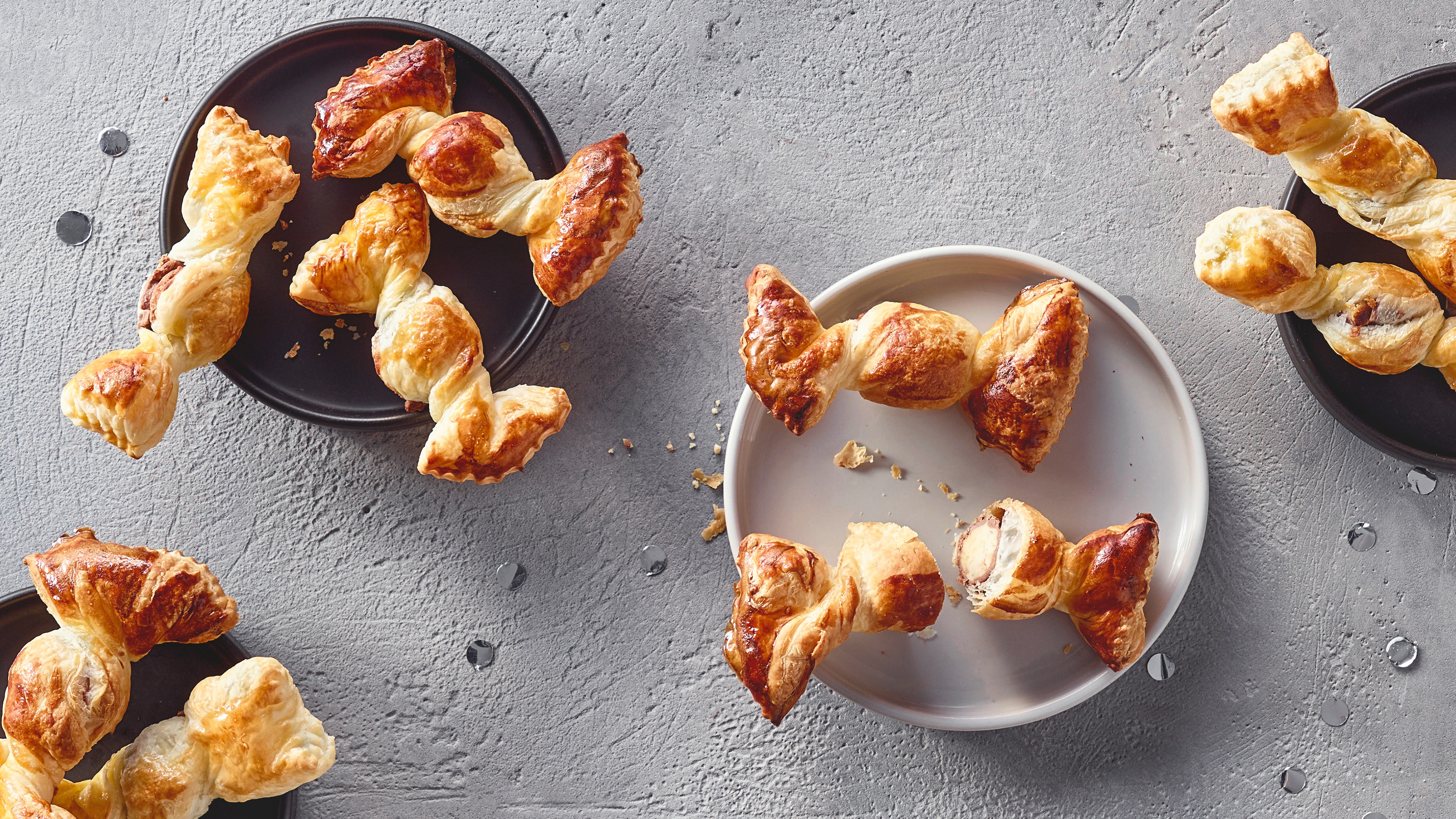 Ein Teller mit gedrehten Blätterteigstücken, goldbraun gebacken und gefüllt mit einer hellen Creme, daneben einige Krümel