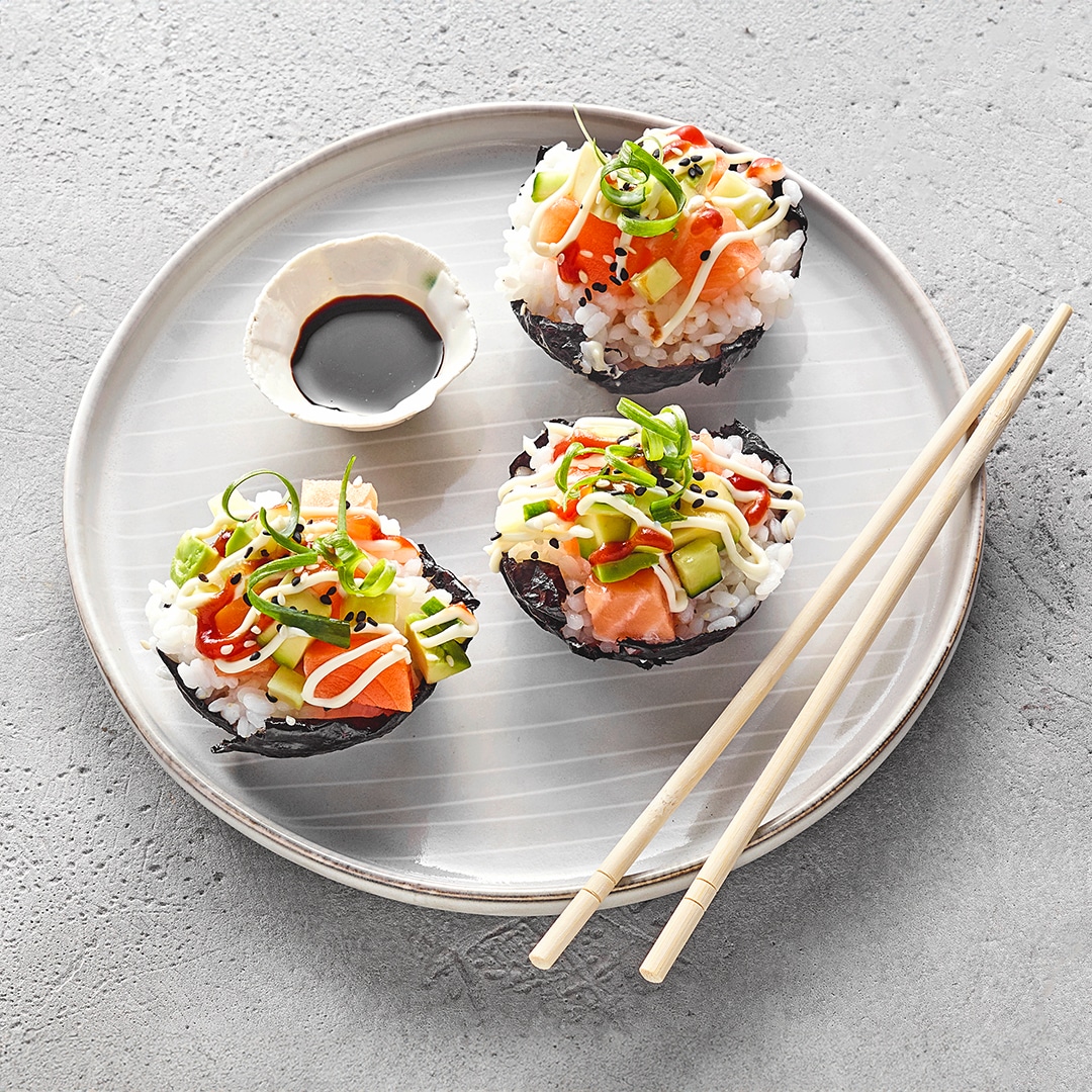Kleine, runde Sushi‑Muffins aus in einer Muffinform gepresstem Reis, belegt mit rohem Lachs, Avocado und Sesam.