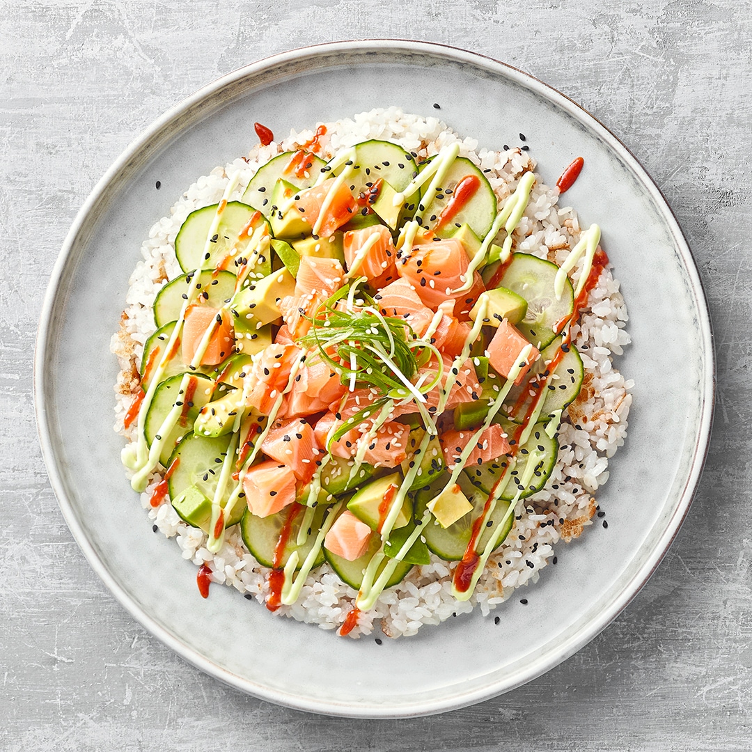 Teller mit in Kreisform gedrückten Reis, Lachs, Avocado und Gurke, garniert mit Sauce und Sesam.