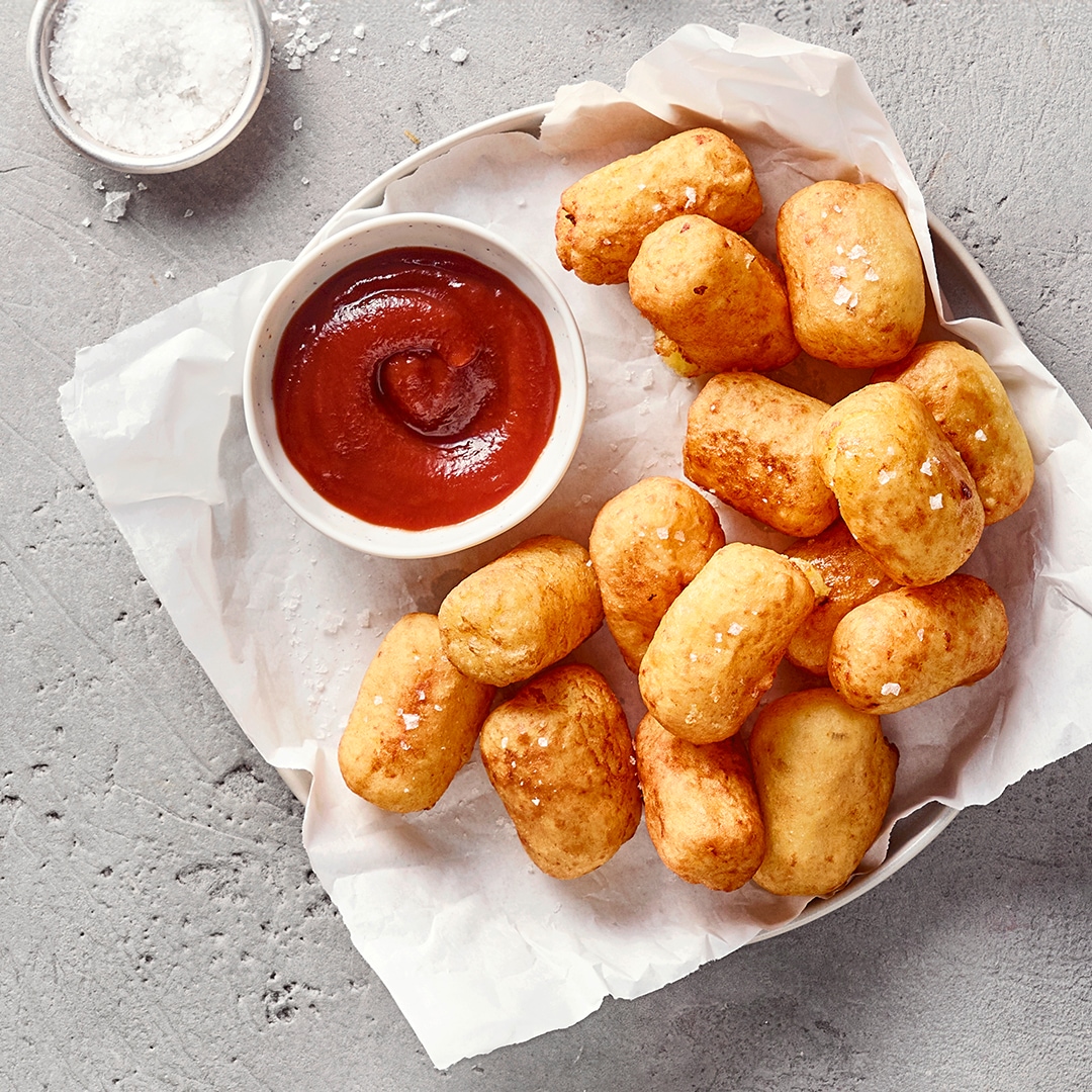 Ein Teller mit goldbraunen Teigbällchen, bestreut mit grobem Salz, dazu eine Schale mit roter Soße.