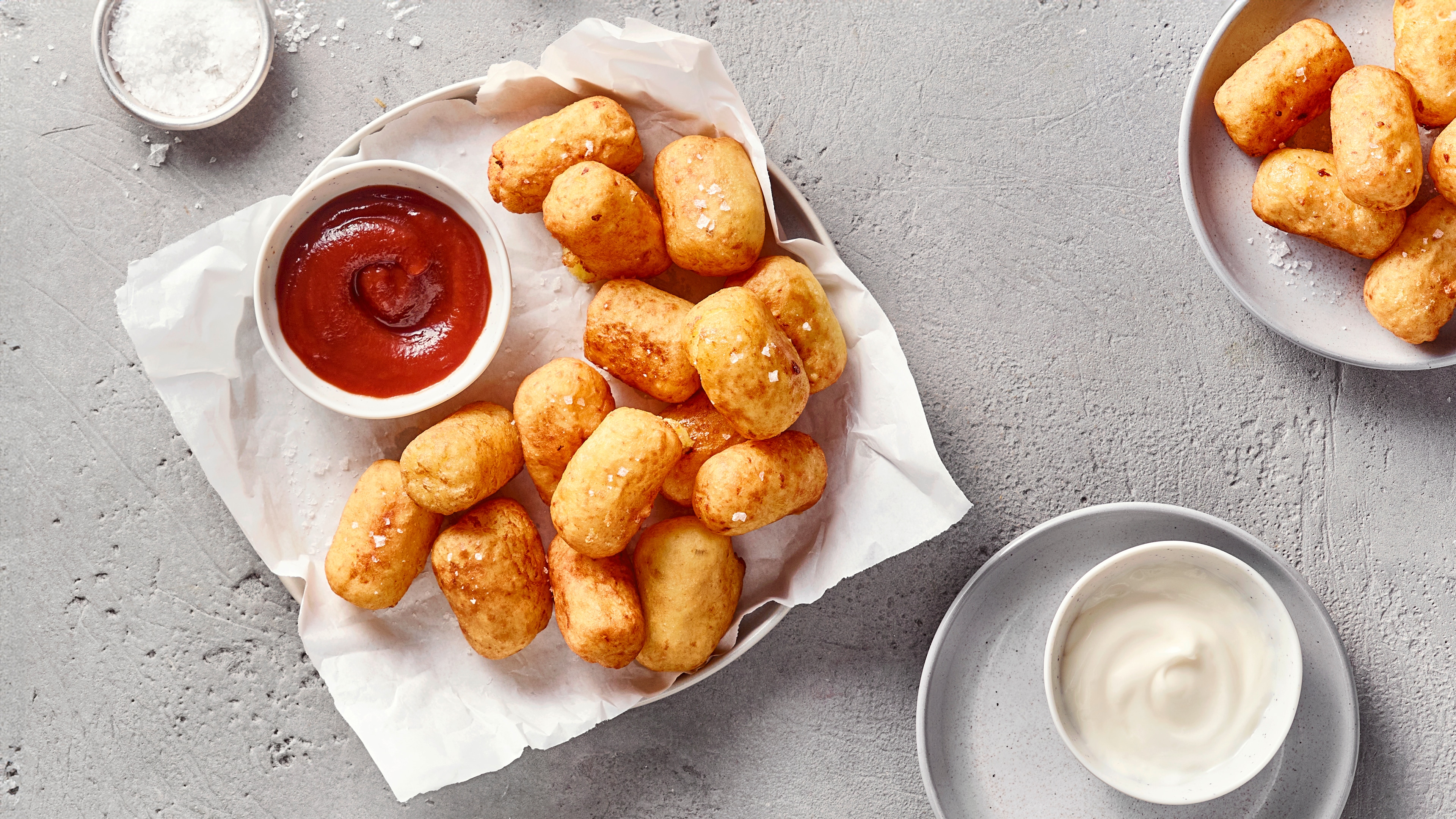 Ein Teller mit goldbraunen Teigbällchen, bestreut mit grobem Salz, dazu eine Schale mit roter Soße.