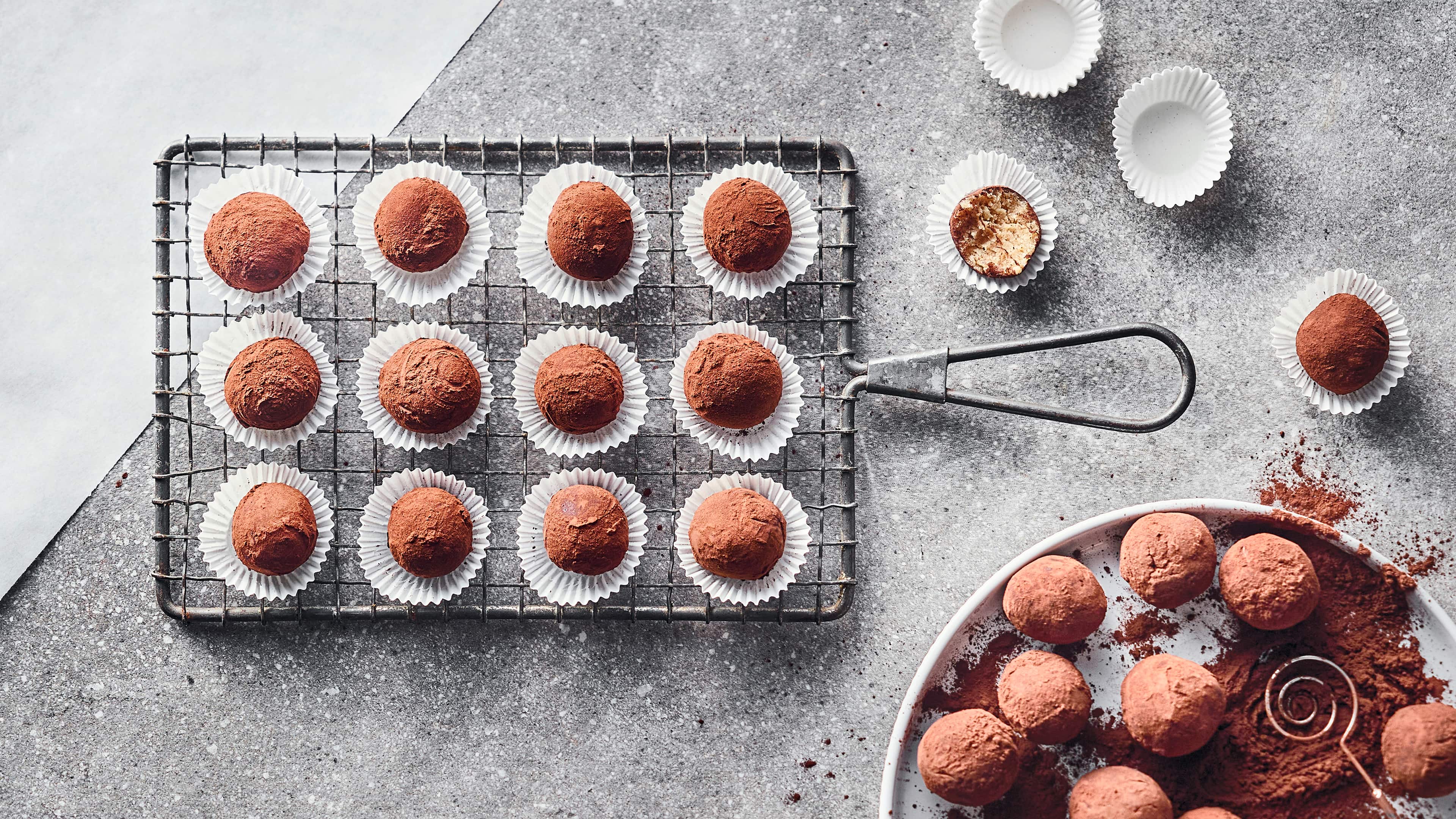 Rezept für Tiramisu-Kugeln Kugelförmige, in Kakao gewälzte Pralinen in kleinen Pralinenförmchen aus Papier auf einem Gitterrost.