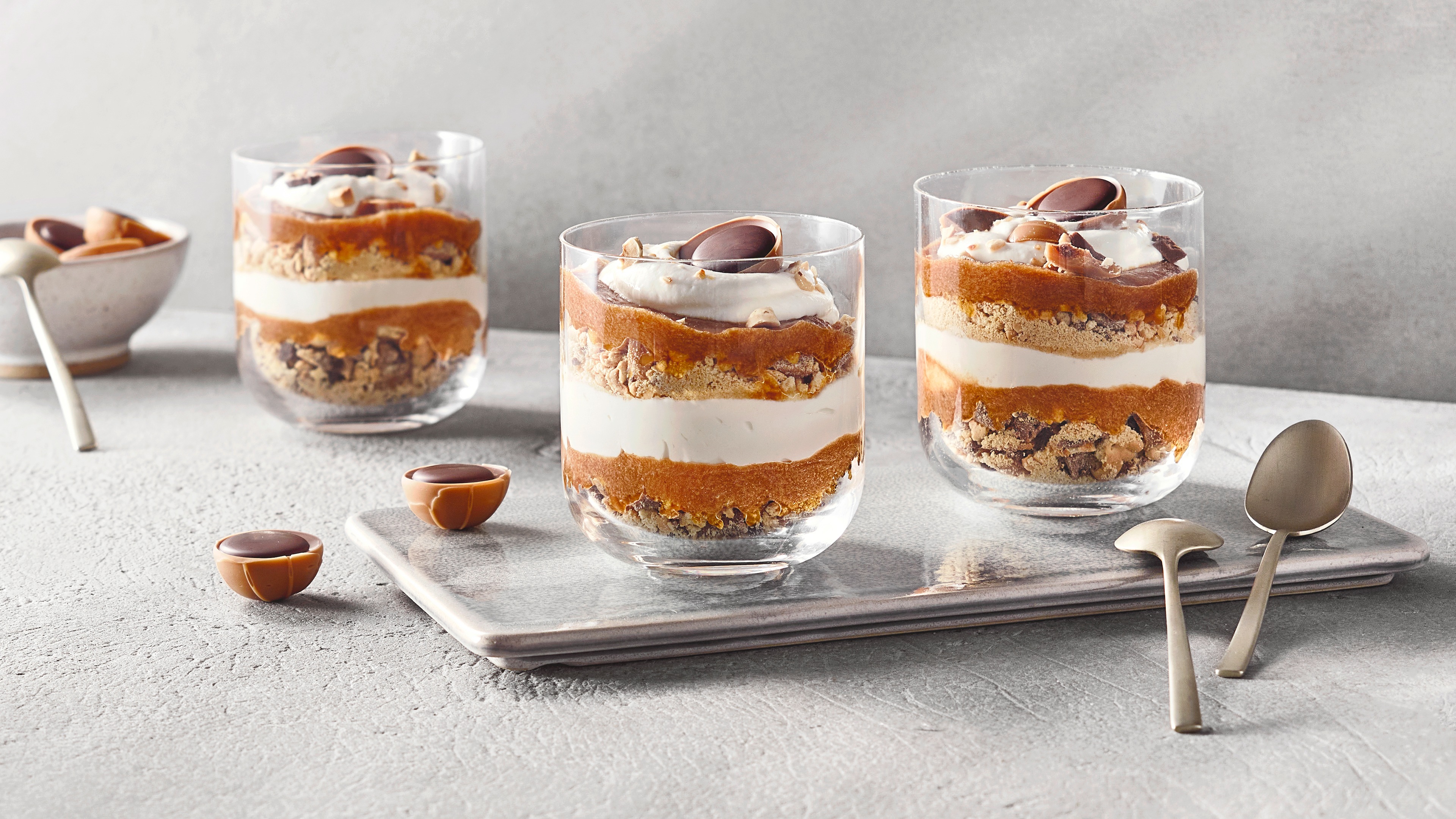 Drei Dessertgläser mit Toffifee-Pralinen und Schichten aus Creme, Keksboden und Karamell.