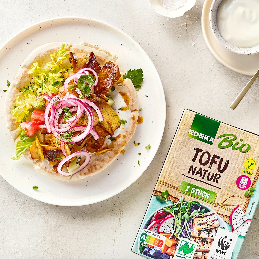 Gefülltes Fladenbrot mit Salat, roten Zwiebeln, Gemüse und gebratenem Tofu auf weißem Teller, serviert mit Joghurt-Dip; daneben EDEKA Bio Tofu Natur.