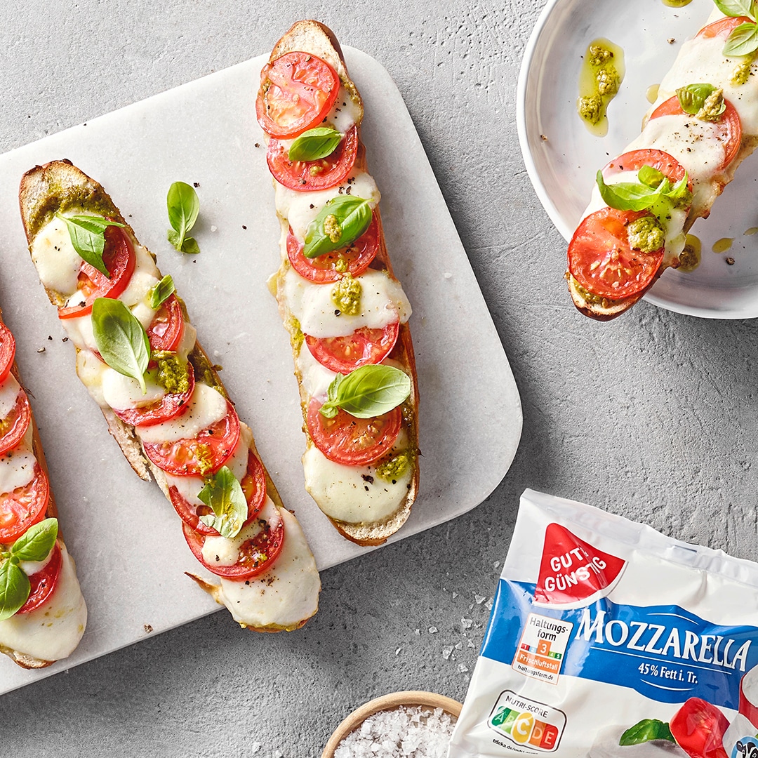 Knusprig gebackene Laugenstangen mit Tomatenscheiben und Mozzarella. Daneben eine Packung Gut&Günstig Mozzarella.