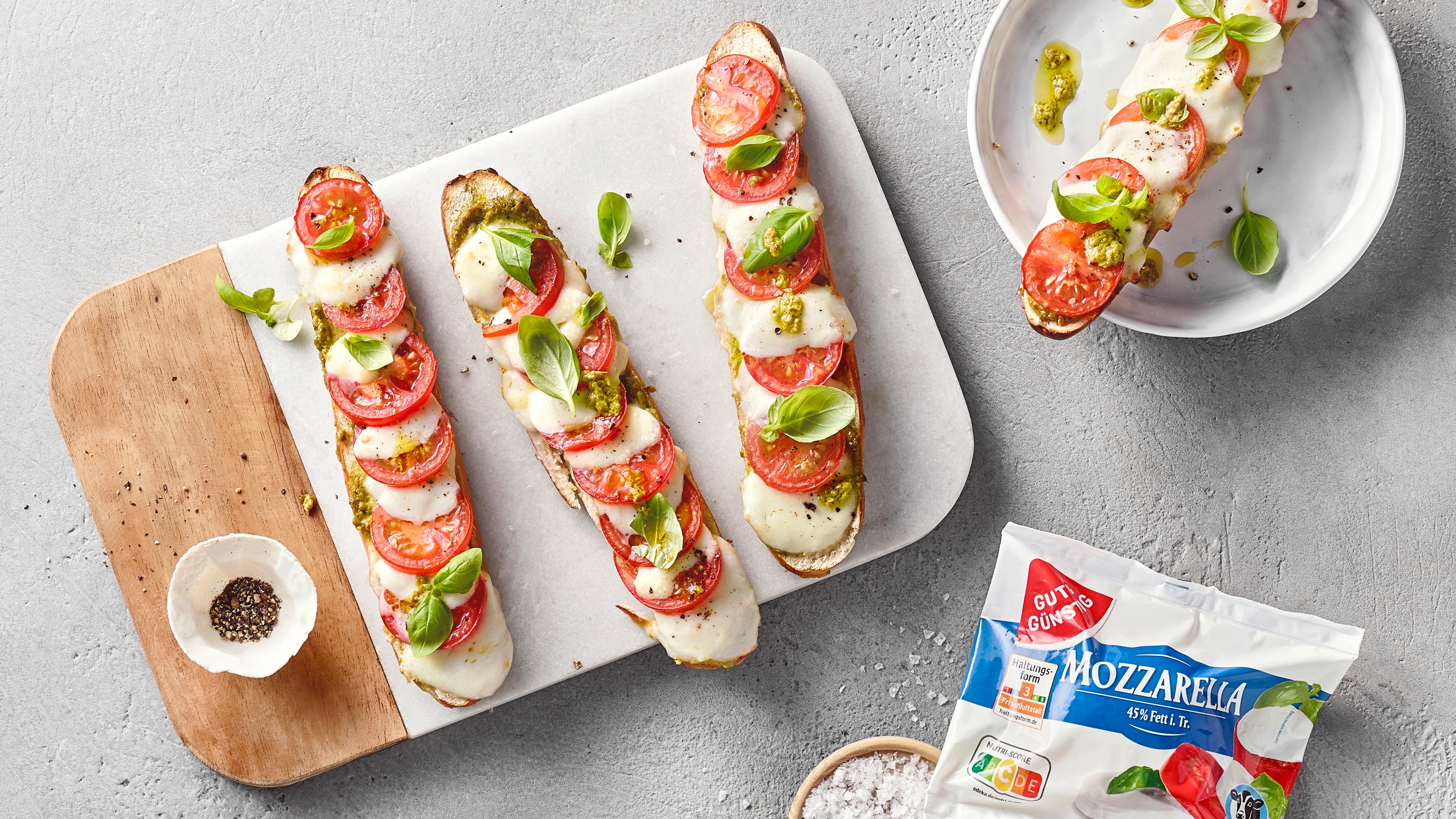 Knusprig gebackene Laugenstangen mit Tomatenscheiben und Mozzarella. Daneben eine Packung Gut&Günstig Mozzarella.