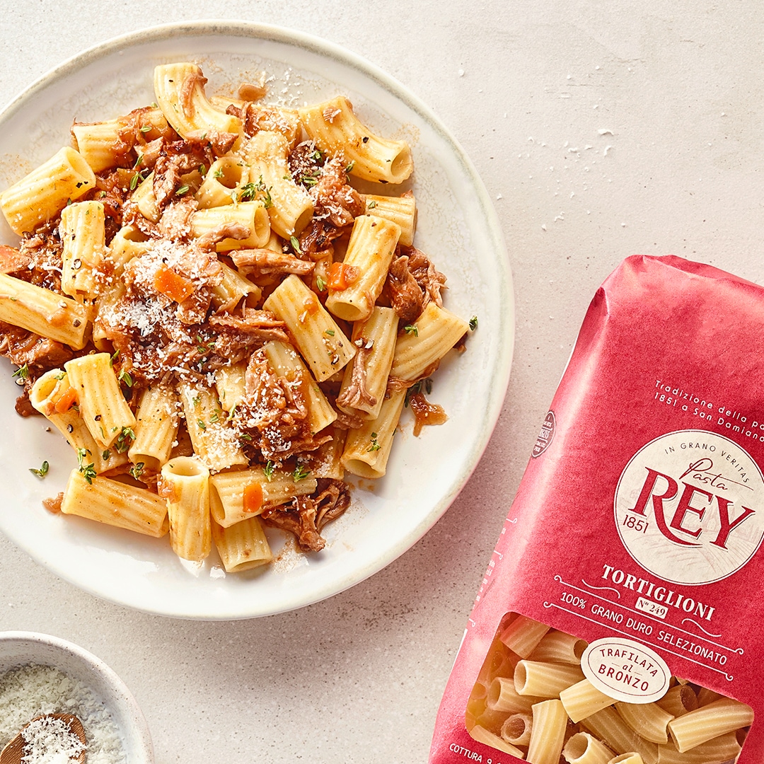 Teller mit Nudeln, Ragout und Parmesan. Daneben eine Packung Pasta Rey Torglioni