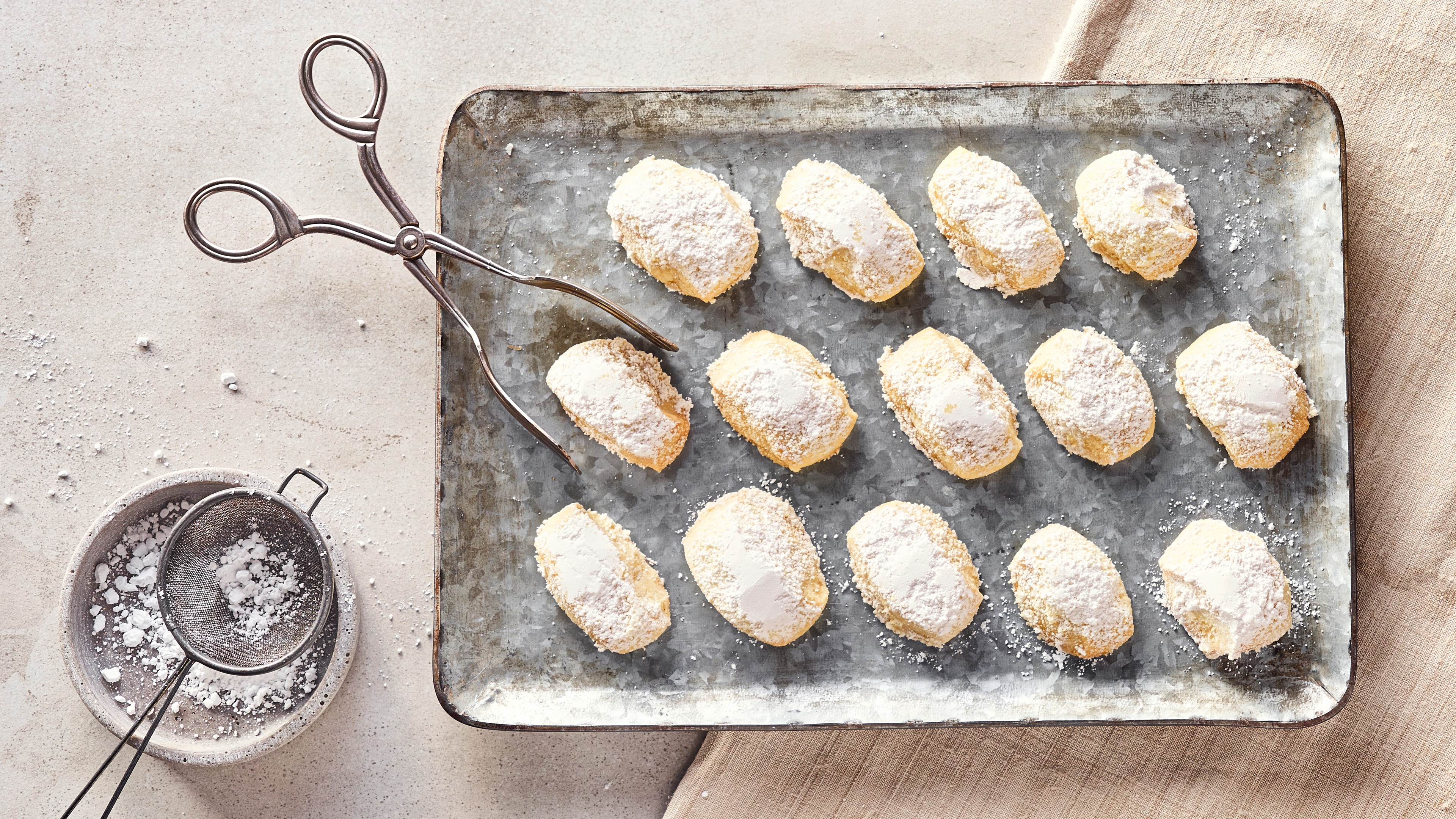 Keks-Rezept für Traumstücke Ovale helle Butterkekse, gewälzt in Puderzucker, auf einem metallischen Backblech