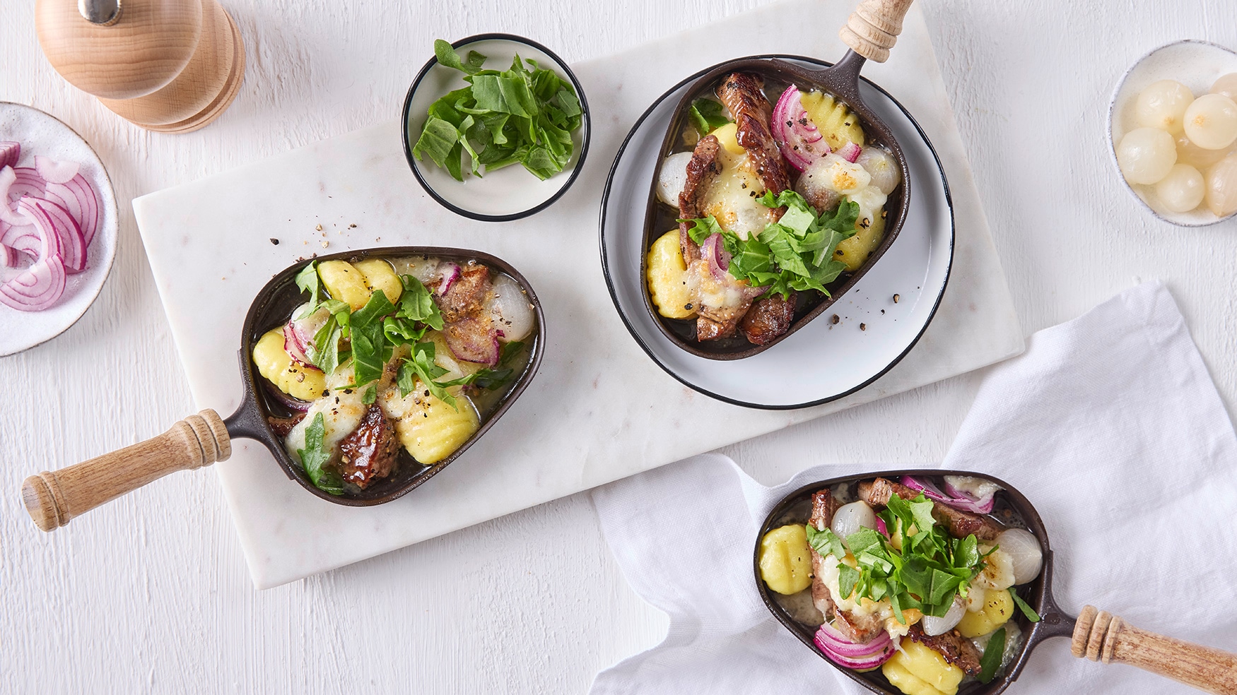 Rezept für Trüffel-Raclette mit Mozzarella usseisenpfännchen mit geschmolzenem Käse, Gnocchi, roten Zwiebeln, Perlzwiebeln und frischen Kräutern