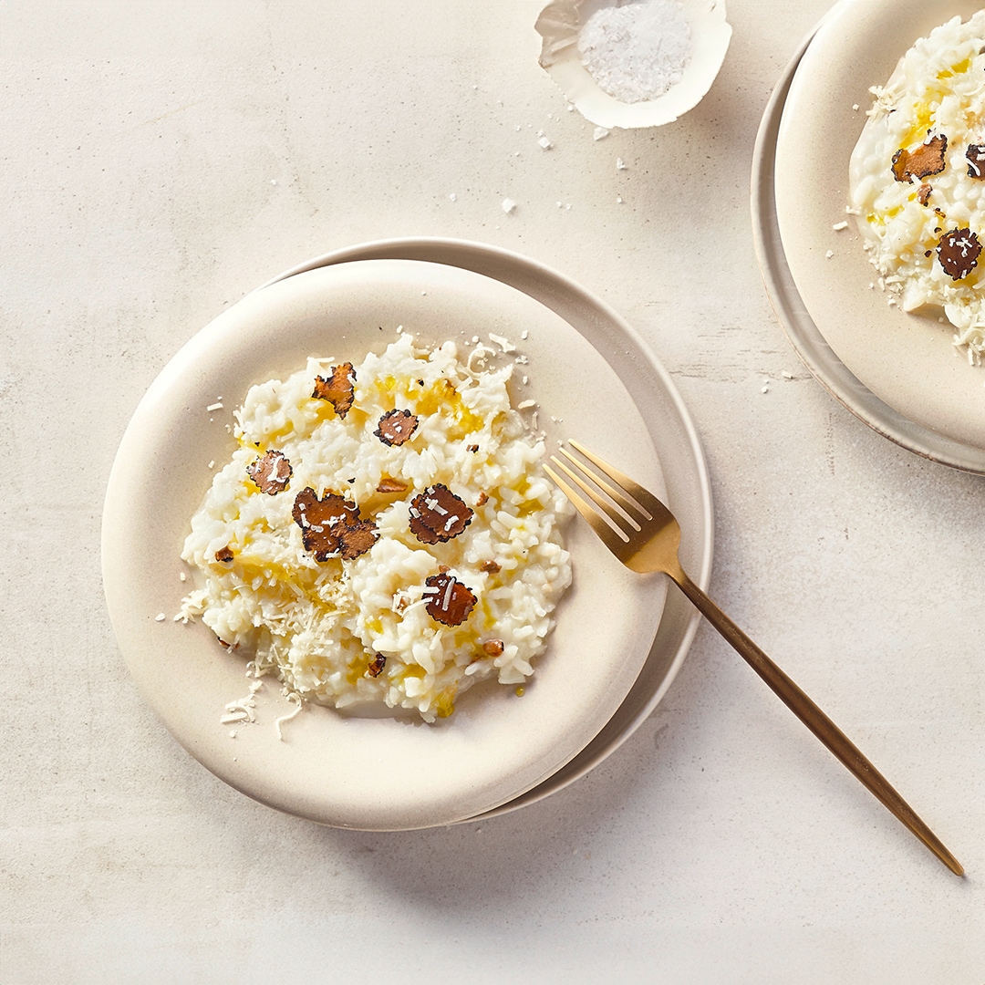 Runde Teller mit cremigem, buttrigem Reis, getoppt mit geriebenem Käse und Trüffelscheiben