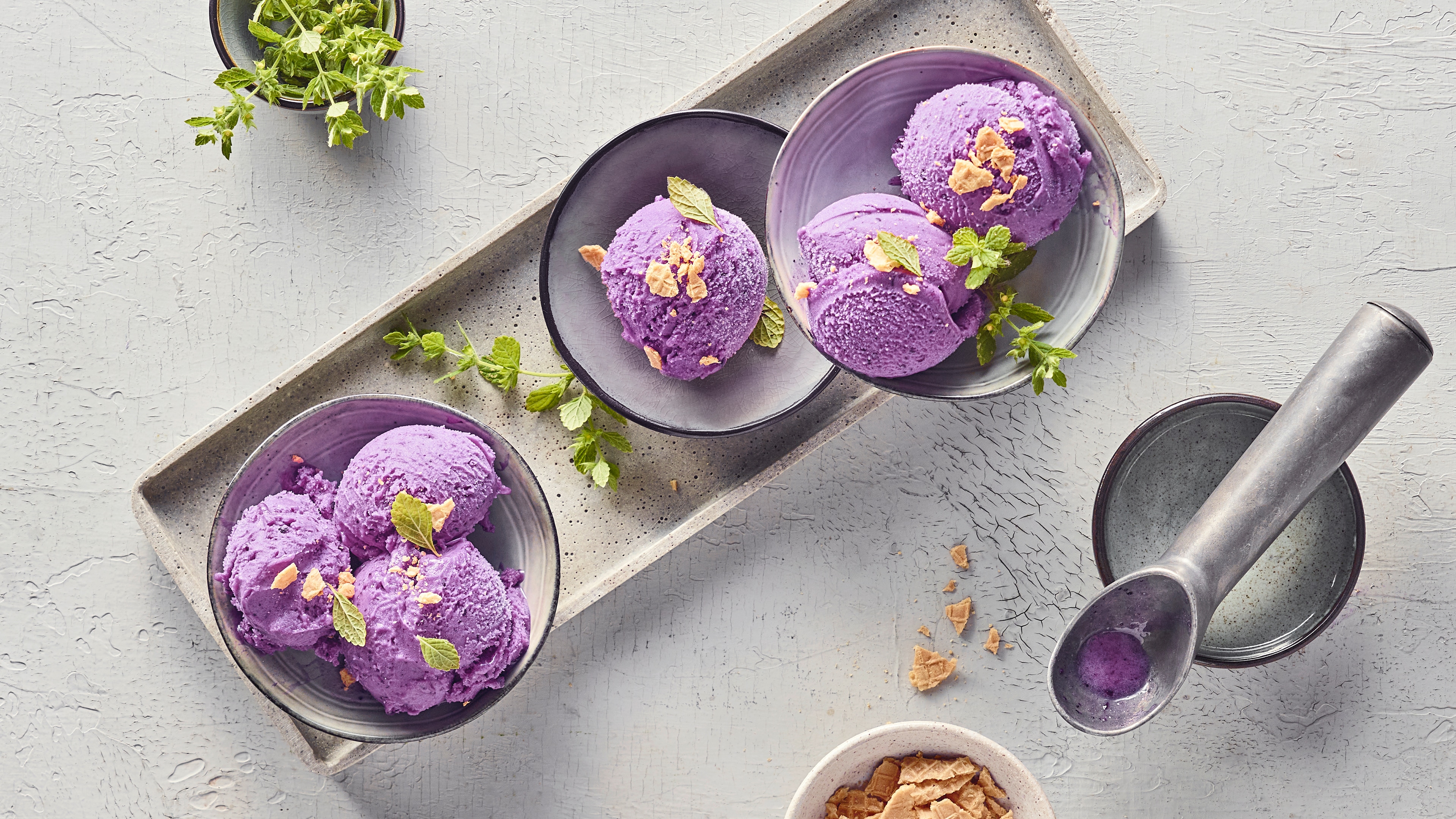 Rezept für Ube Eis Kleine Schüsseln mit kräftig lila Eiskugeln, getoppt mit frischer Minze und Eiswaffelbruch