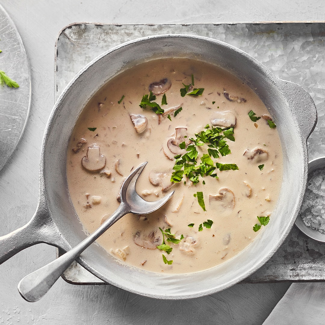 Eine gusseiserne Pfanne mit cremiger heller Pilzsauce, garniert mit frischer Petersilie.