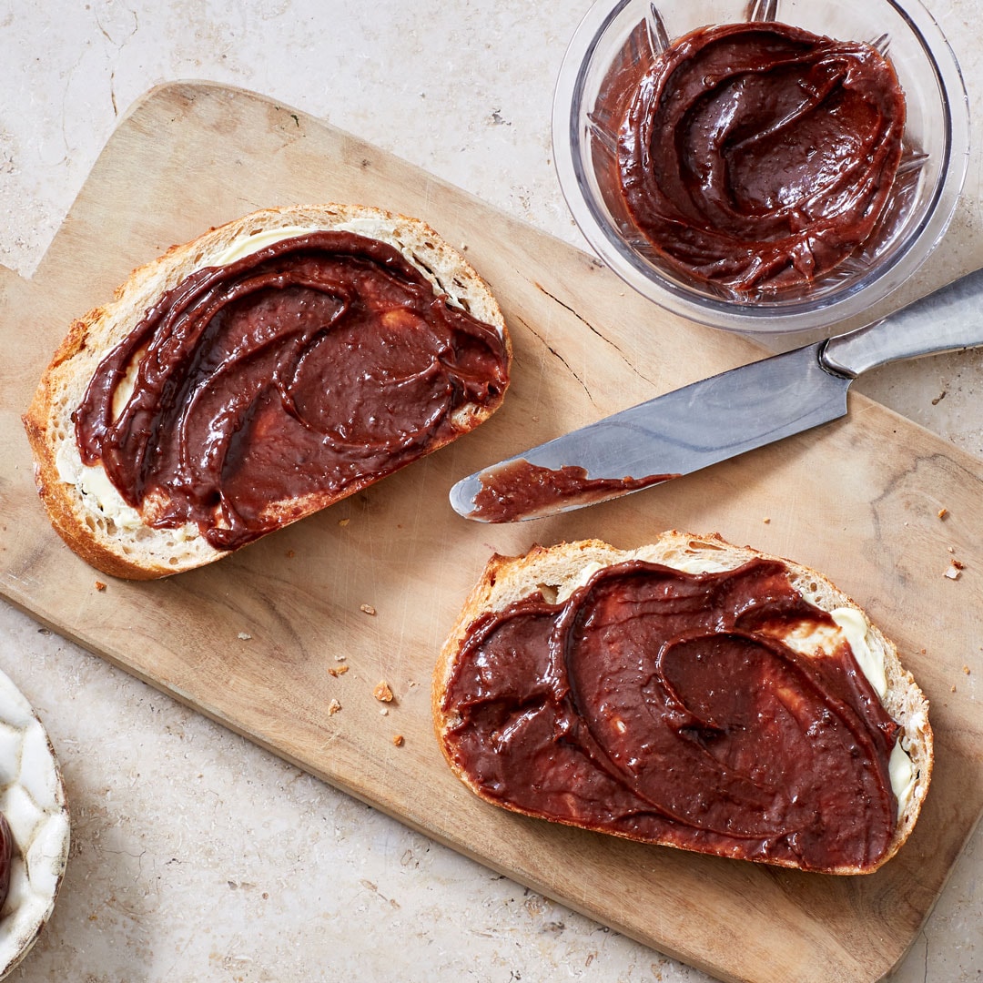 Mit dunkler Creme geschmierte Brotscheiben auf Holzbrett