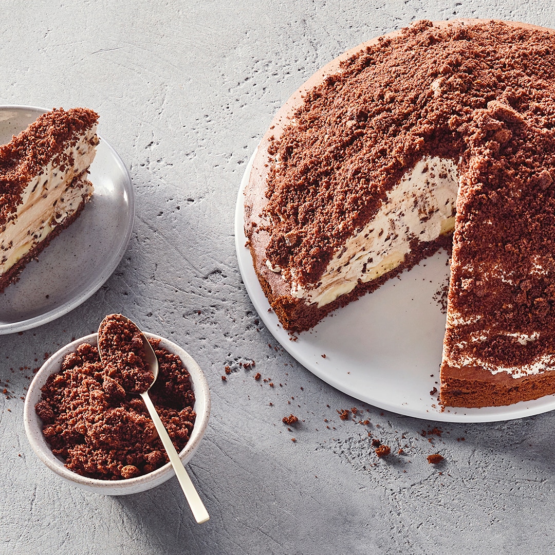 Hügeliger Kuchen mit Kakaobröseln, daneben ein Stück auf einem Teller und Kakaobrösel im Schälchen