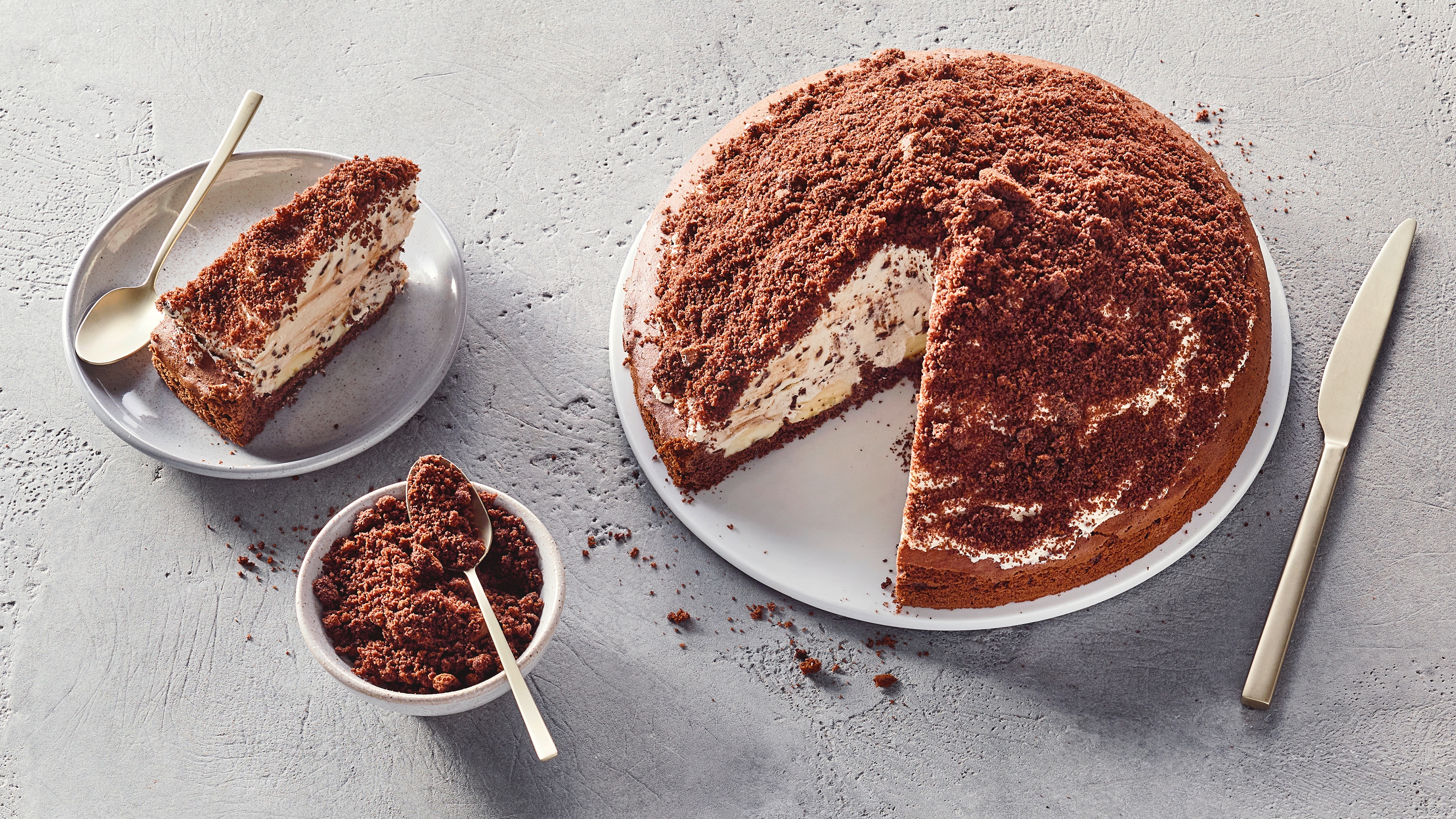 Hügeliger Kuchen mit Kakaobröseln, daneben ein Stück auf einem Teller und Kakaobrösel im Schälchen
