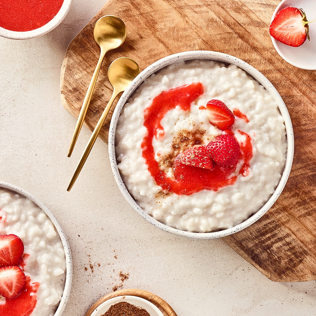 Eine Schale mit cremigem reis, getoppt mit roter Soße, frischen Erdbeeren und einer Zimt-Zucker-Mischung