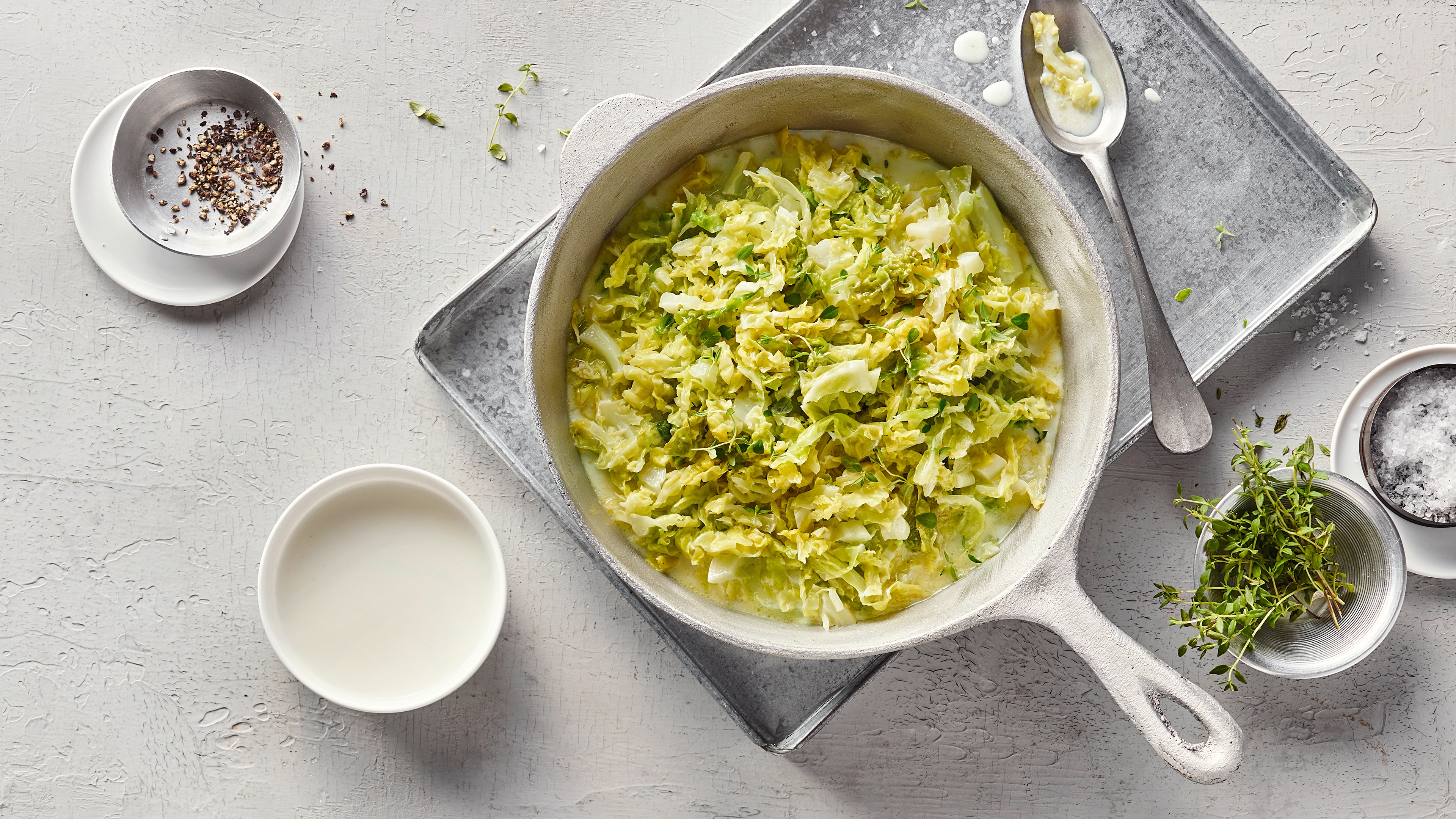 Rezept für veganen Wirsing Ein gusseiserner Topf mit Wirsingkohl in weißer, cremiger Soße, getoppt mit frischem Thymian