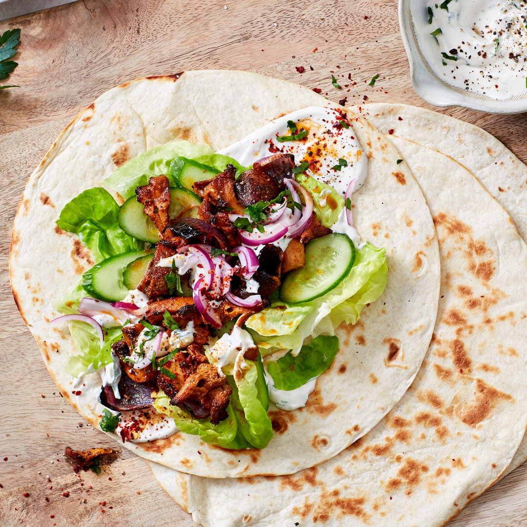 Wraps mit Salat, Gurke, Zwiebeln und gewürzten Pilzen auf Holzbrett, daneben ein heller Dip