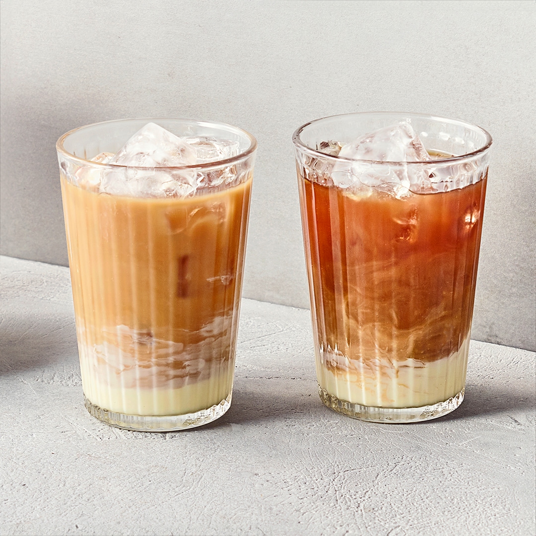 Ein Glas mit braunem Eiskaffee und einem hellen Milchboden, gefüllt mit Eiswürfeln und leicht marmorierter Schichtung.