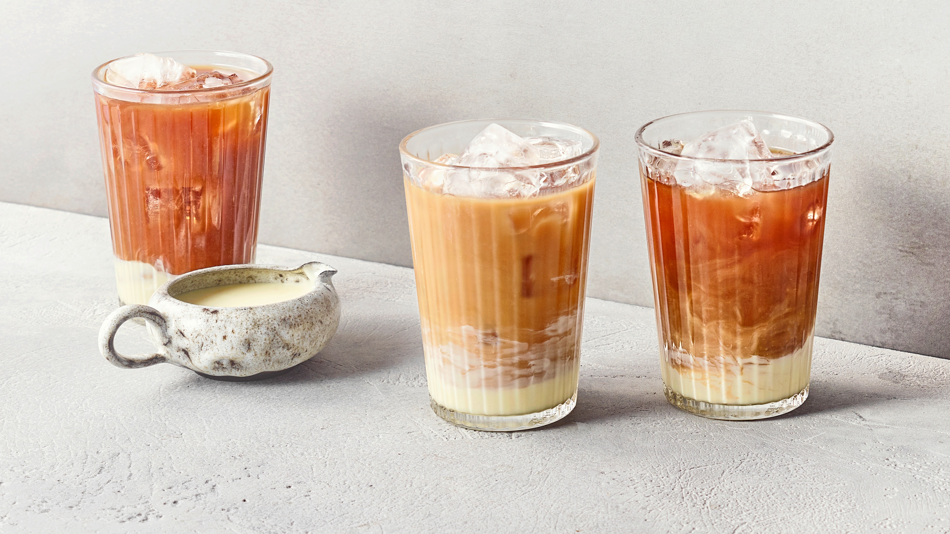 Ein Glas mit braunem Eiskaffee und einem hellen Milchboden, gefüllt mit Eiswürfeln und leicht marmorierter Schichtung.
