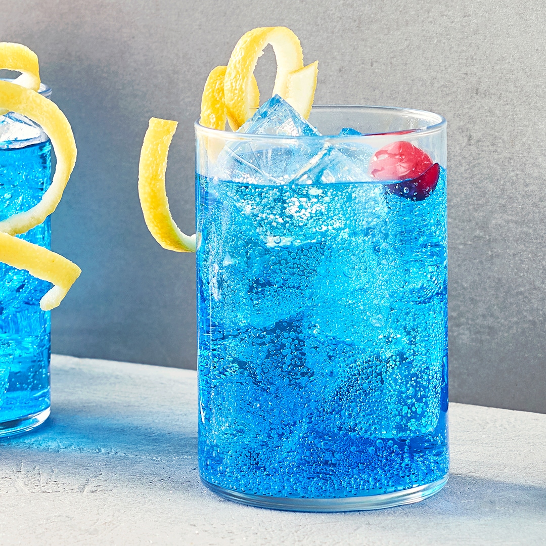 Glas mit blauer Flüssigkeit, Eiswürfel, Kirsche und Zitronenzeste