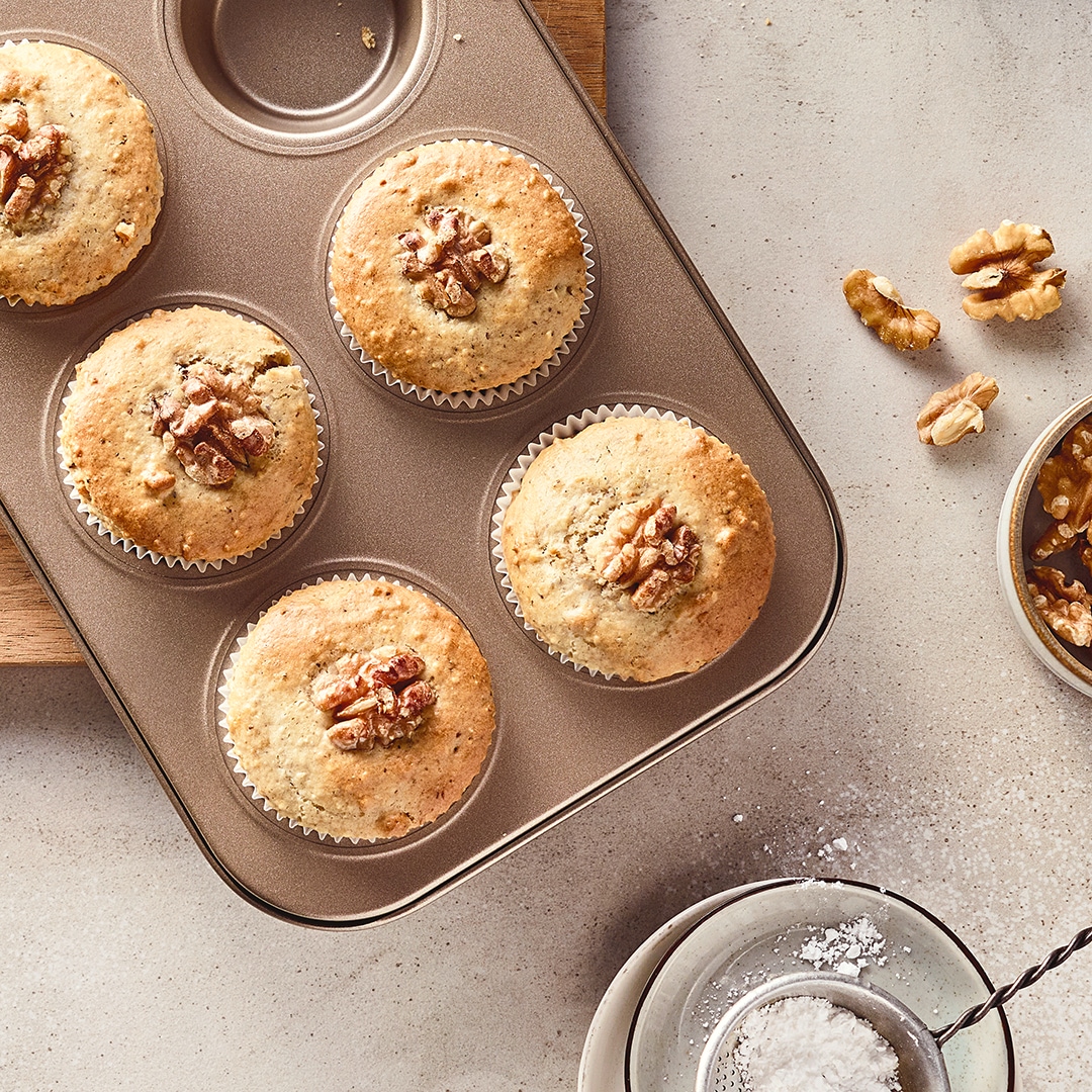 Helle, gelbgold gebackene Muffins, getoppt mit ganzen Walnüssen, in einer Muffinbackform