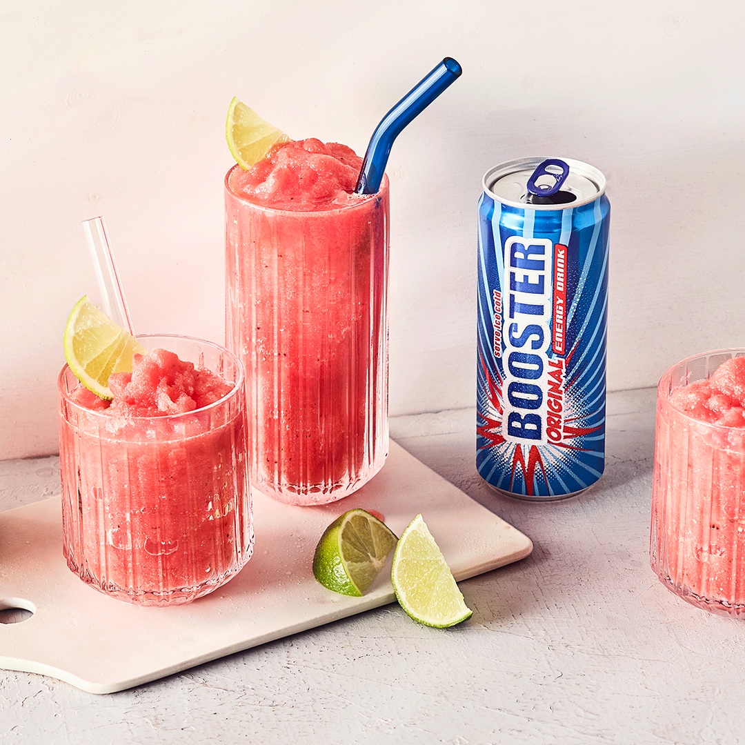 Gläser mit halbgefrorenen hellroten Getränk, Limetten und Glasstrohhalmen, daneben eine Dose Booster Original Energy Drink