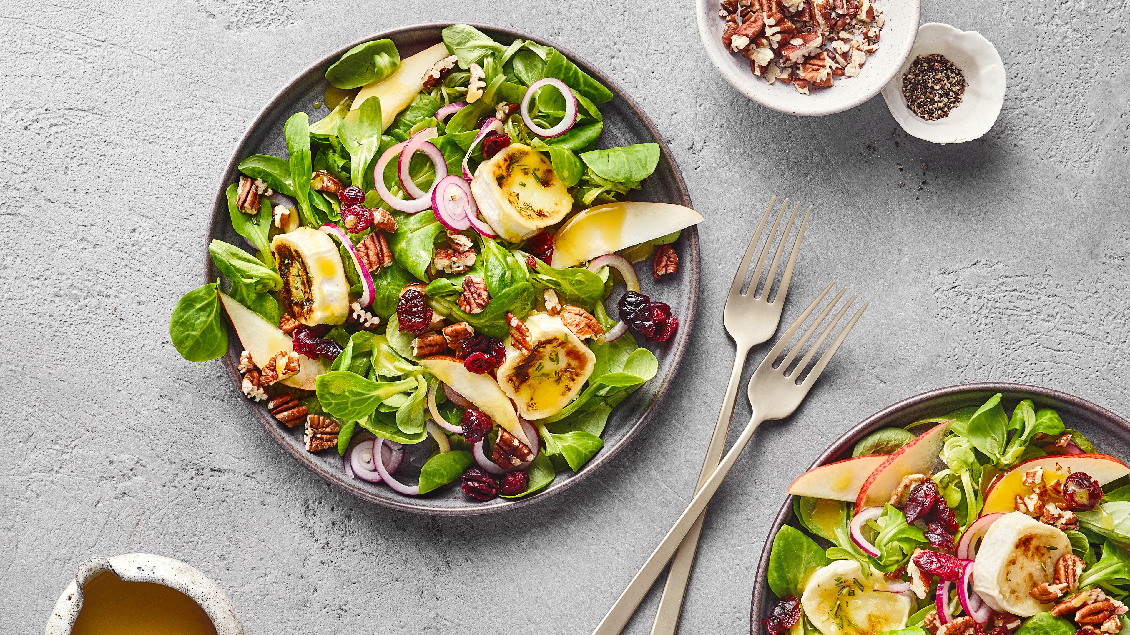 Zwei Salatteller mit Feldsalat, gebratenen Bananenstücken, Apfelstücken, Cranberries, Zwiebeln und Pekannüssen.